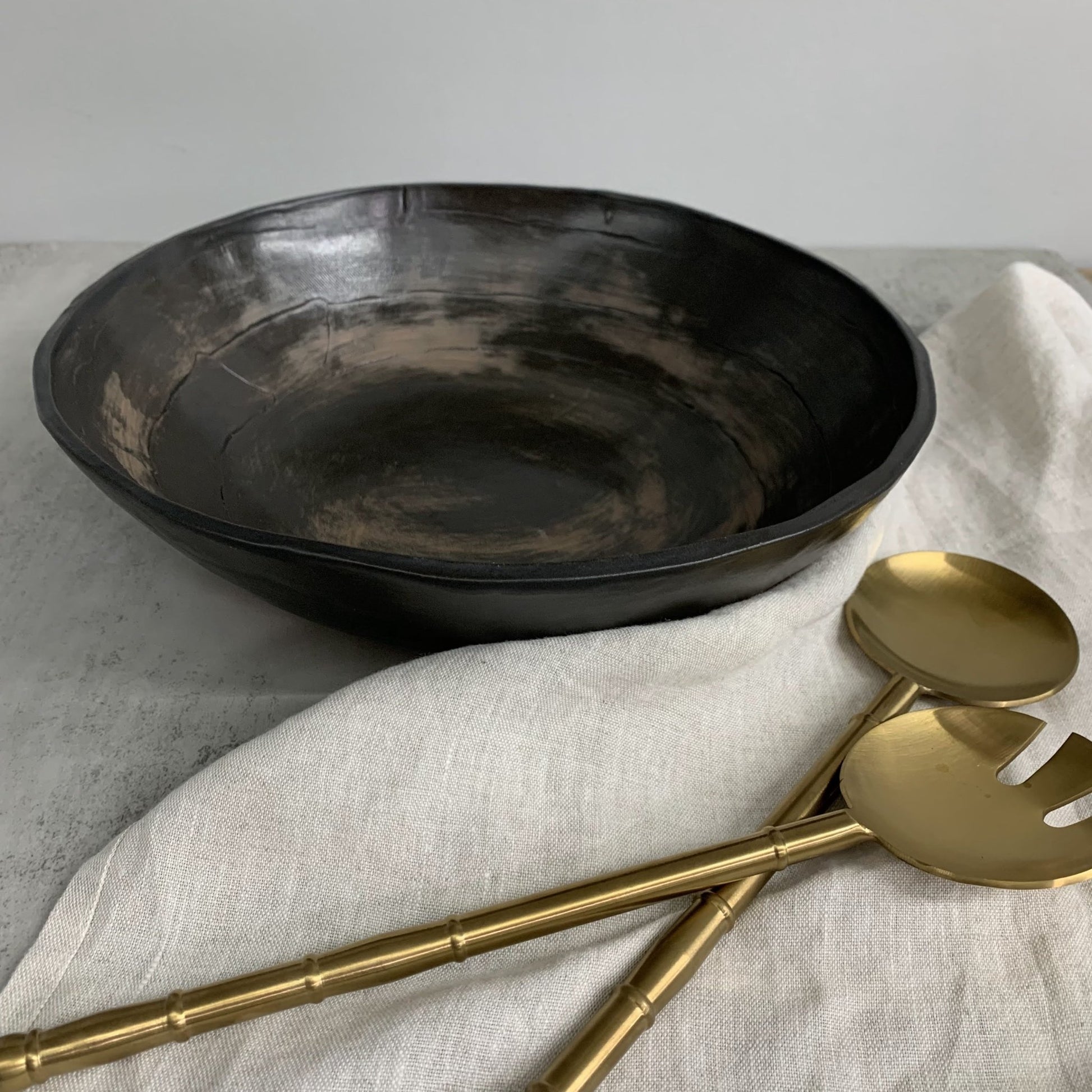 Black ceramic bowl and gold utensils on a light fabric surface