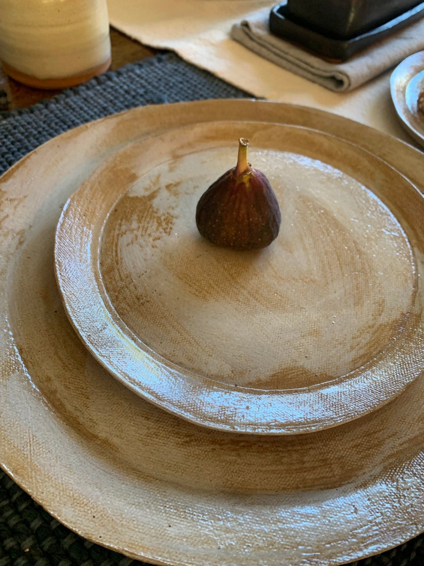 Stack of artisan ceramic plates with a fig on top, placed on a textured surface.