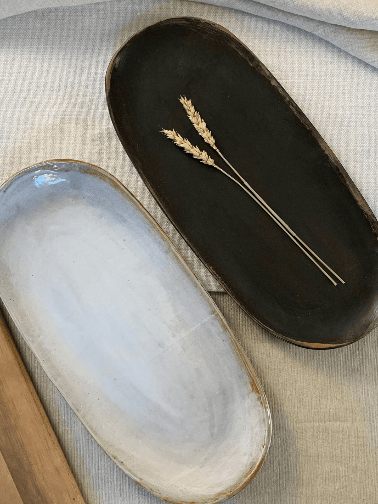 Two handmade ceramic trays, one black and one white with gold rim, on a textured surface.