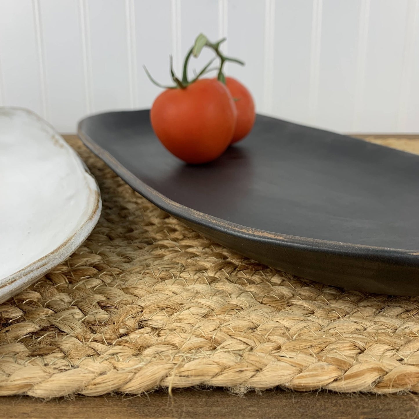 Black handmade stoneware with two tomatoes on a woven placemat