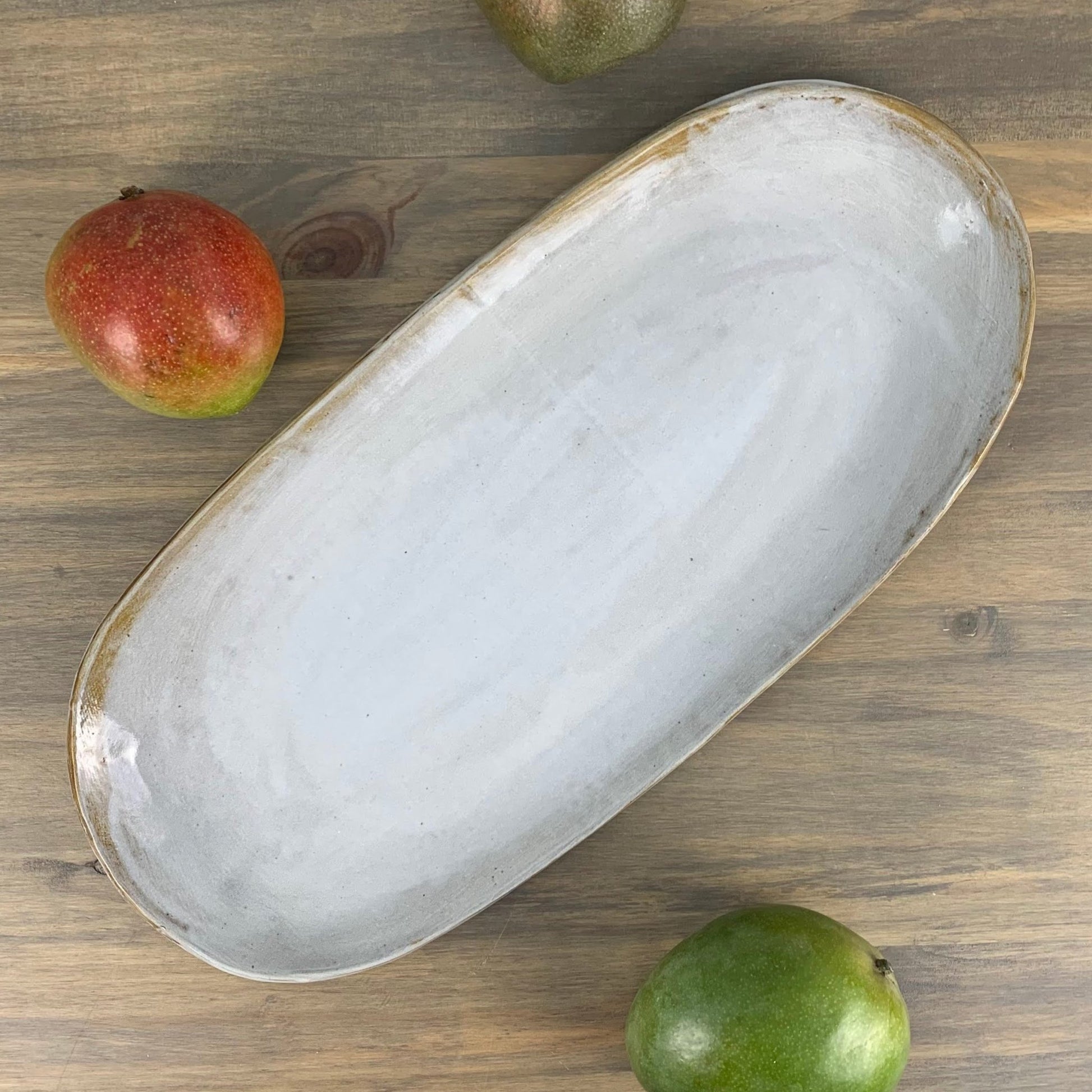 Oval ceramic tray on a wooden surface with pears around it