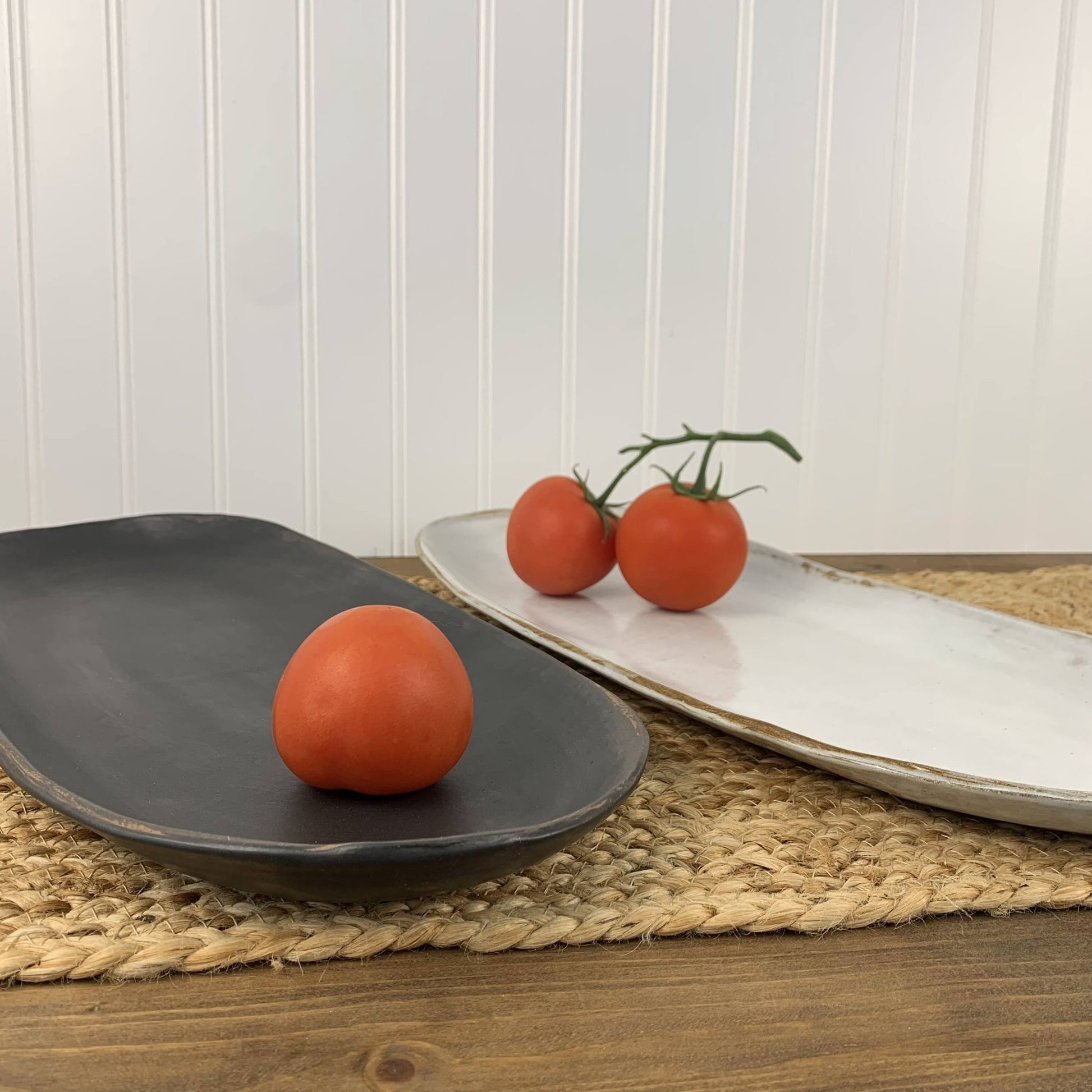 Tomatoes on black and white stoneware on a wooden surface with a white paneled wall background.
