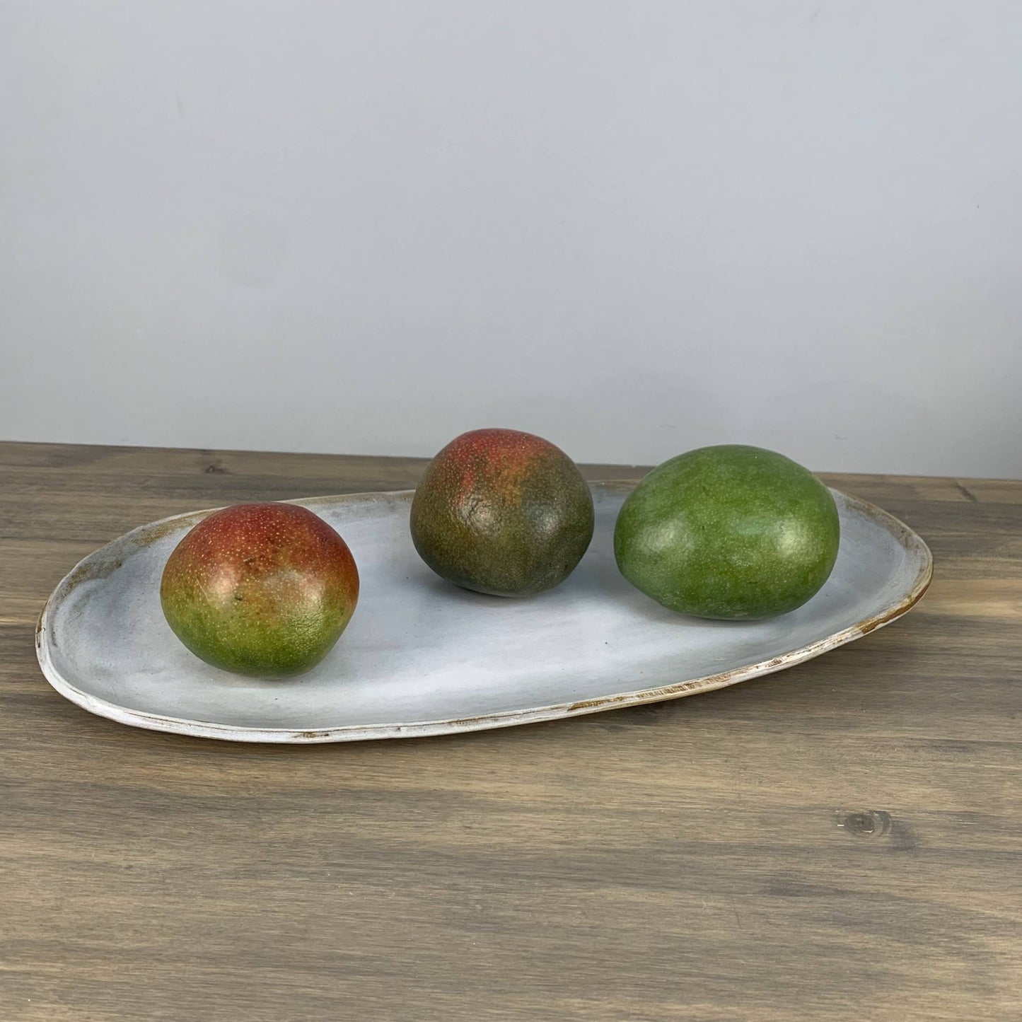 Three mangoes on a white ceramic tray with a plain background