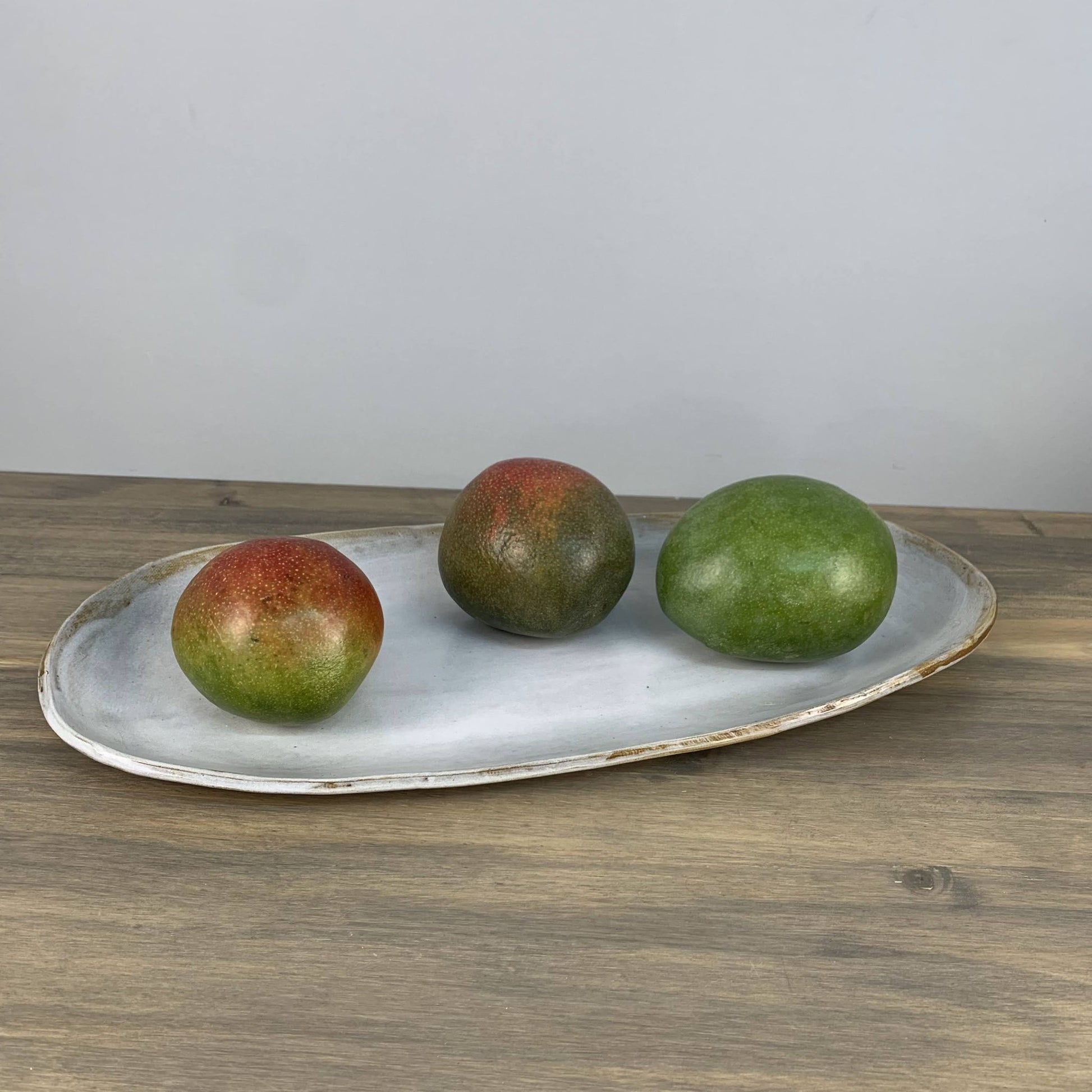 Three mangoes on a white ceramic tray with a plain background