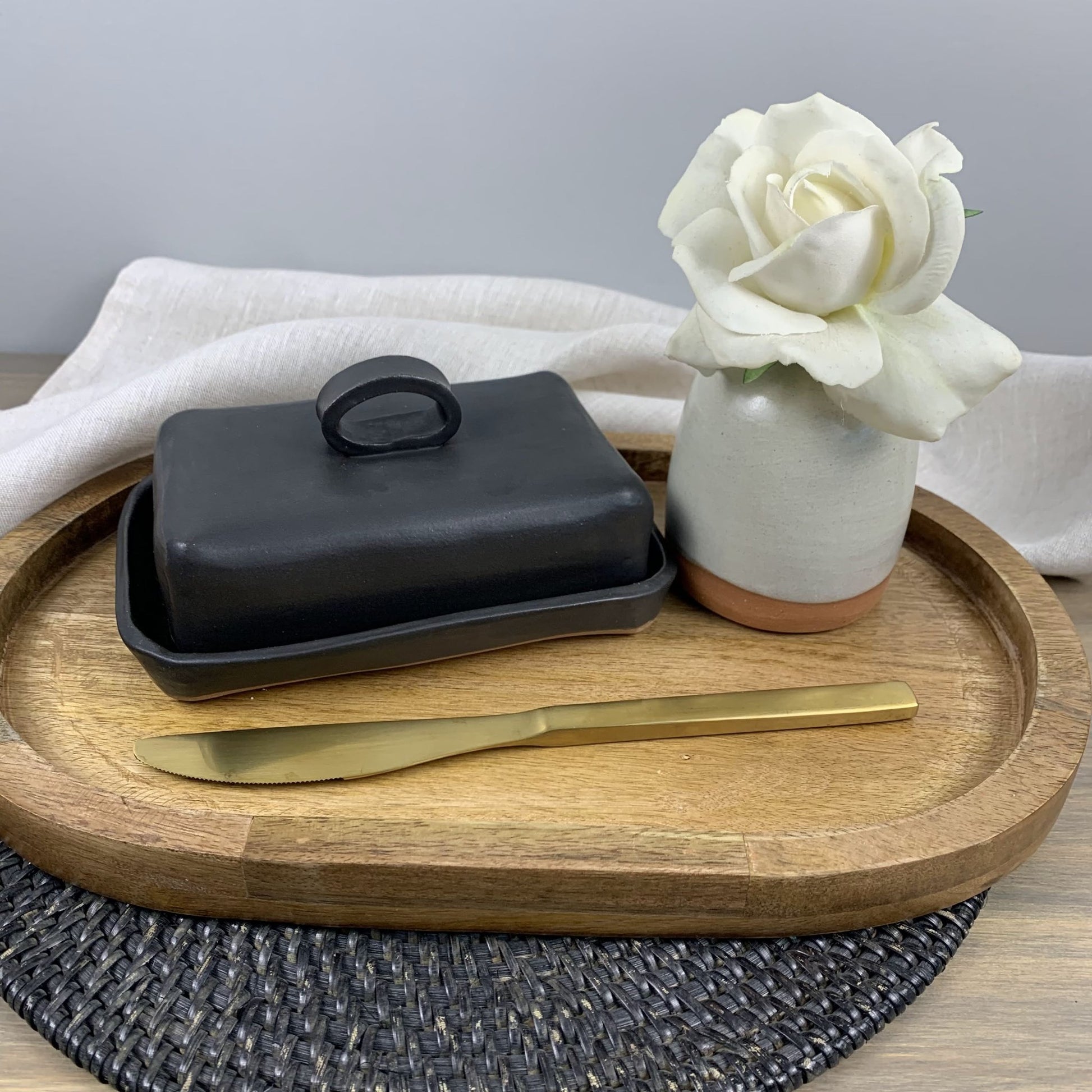 Black butter dish with gold knife on a wooden tray, white rose in the background