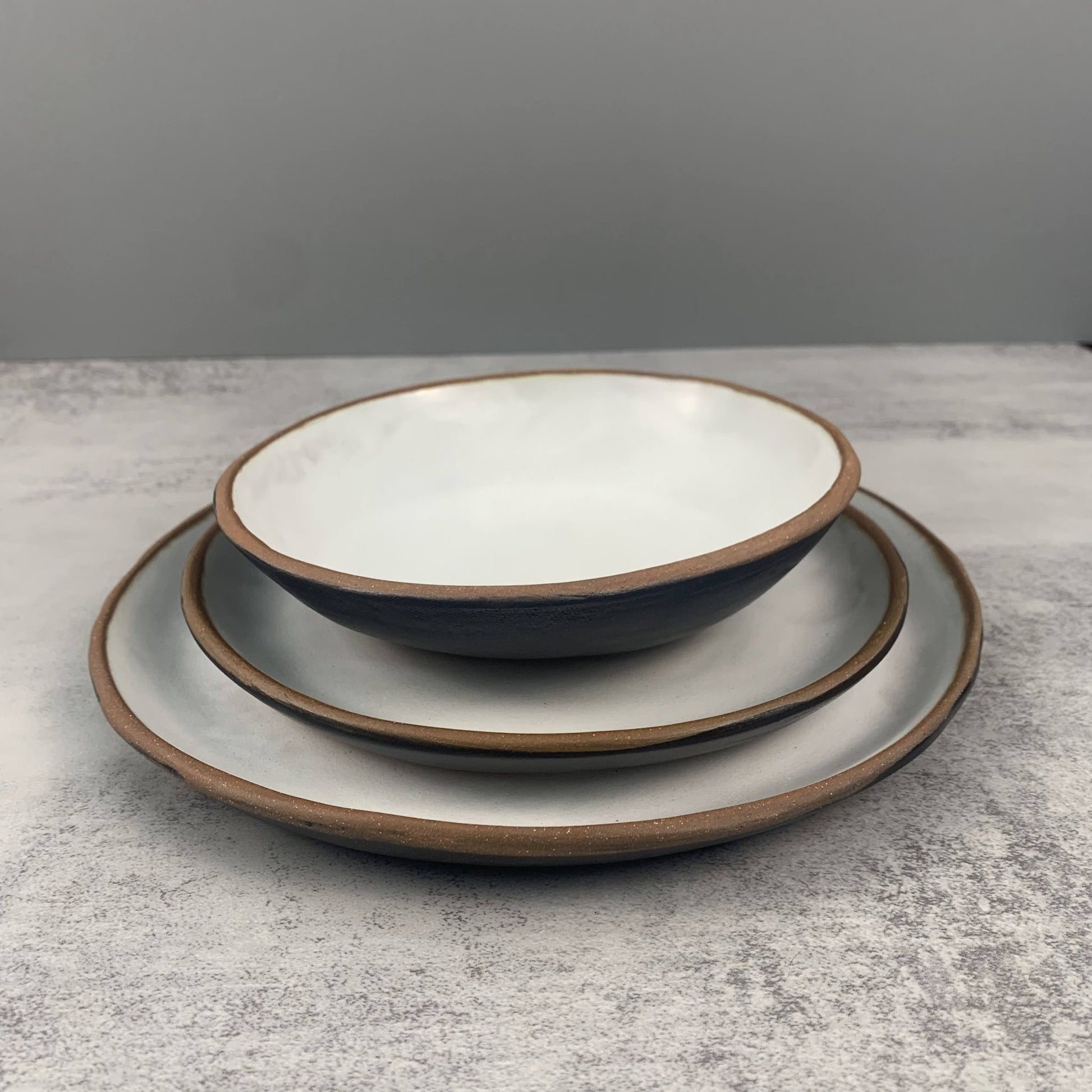 Set of three handmade ceramic bowls stacked on a gray surface with a gray background
