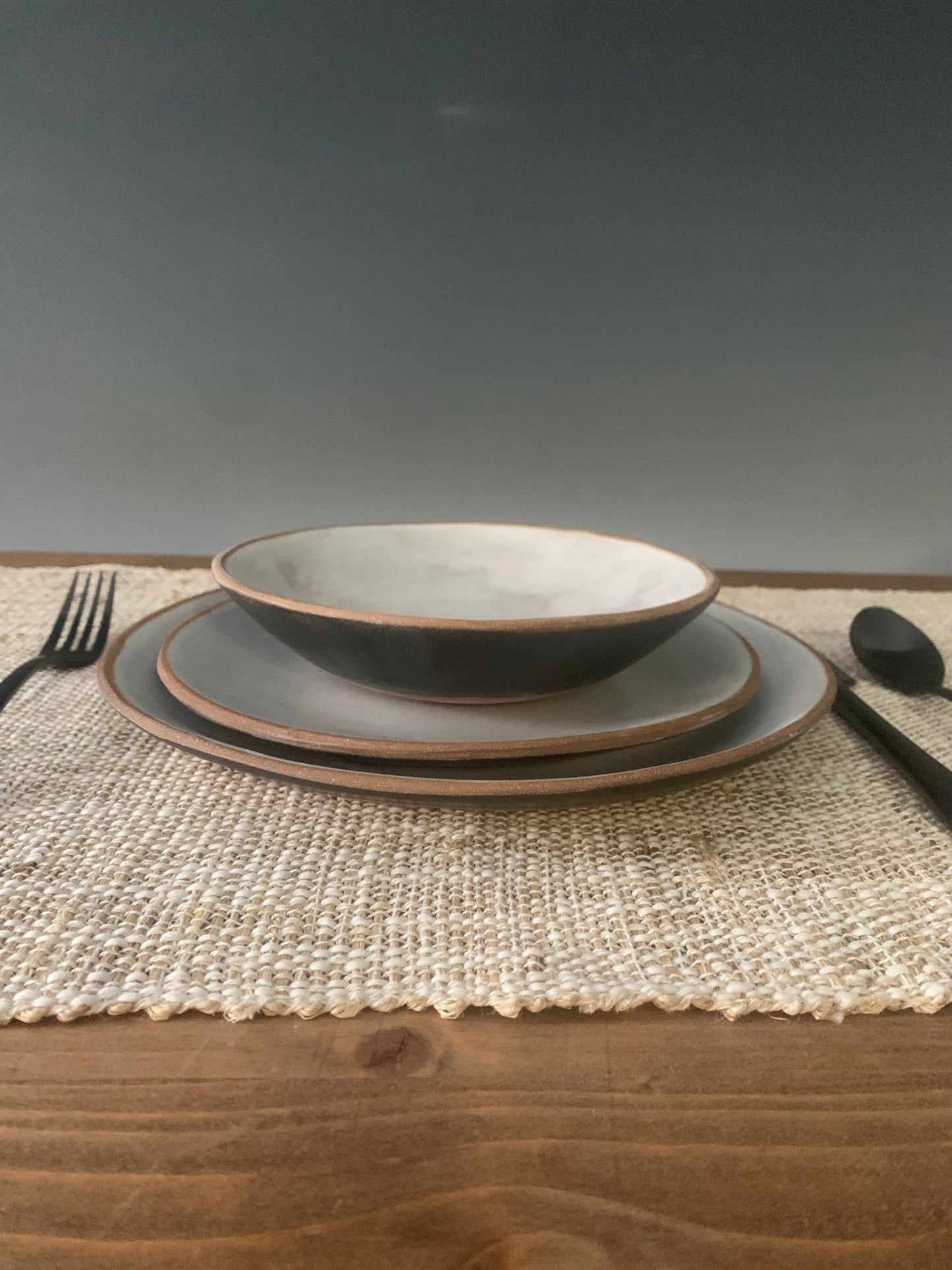 Set of handmade ceramic bowls on a textured placemat with cutlery on a wooden surface.