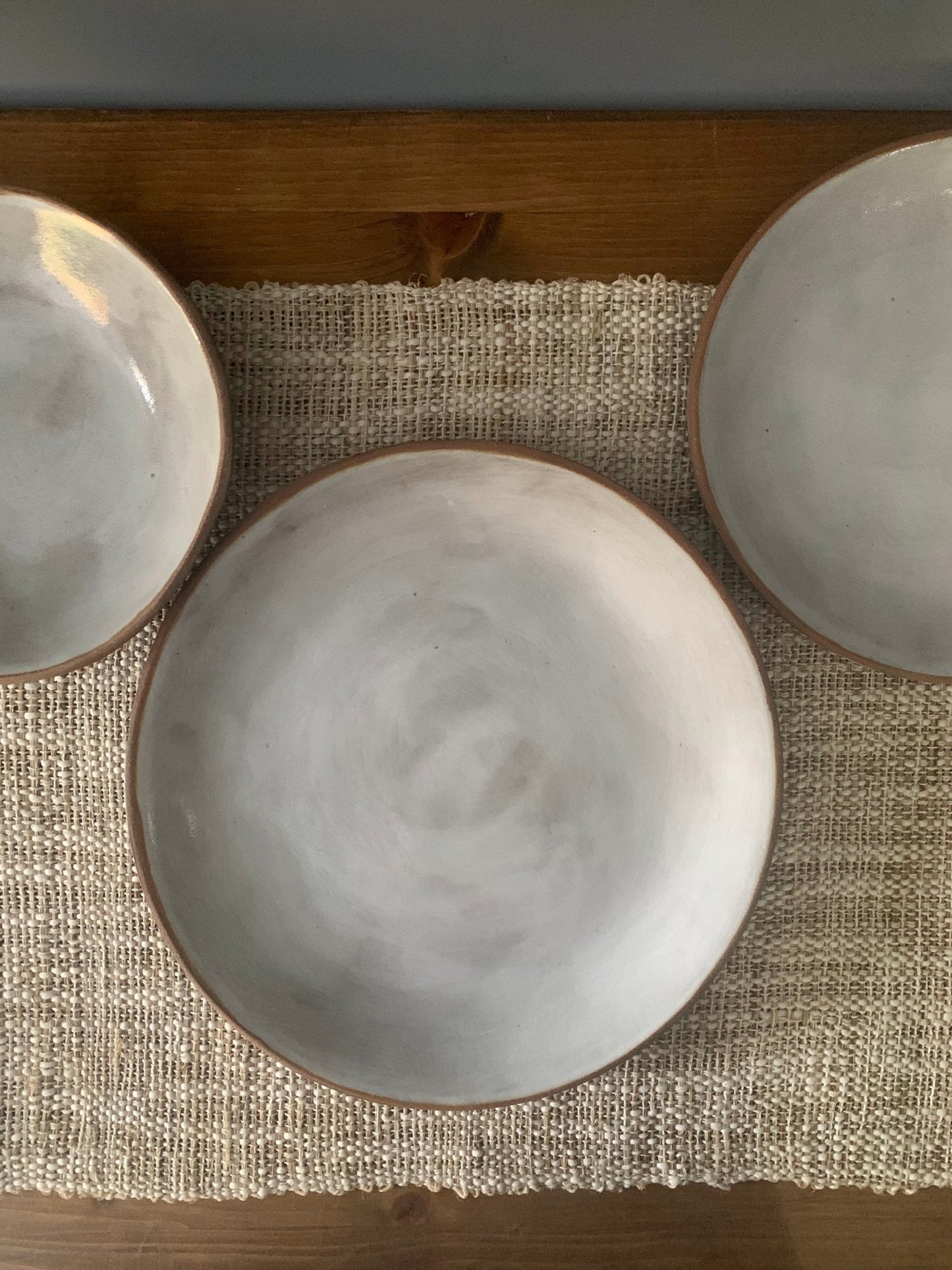 Three handmade ceramic plates on a textured placemat with a wooden surface.