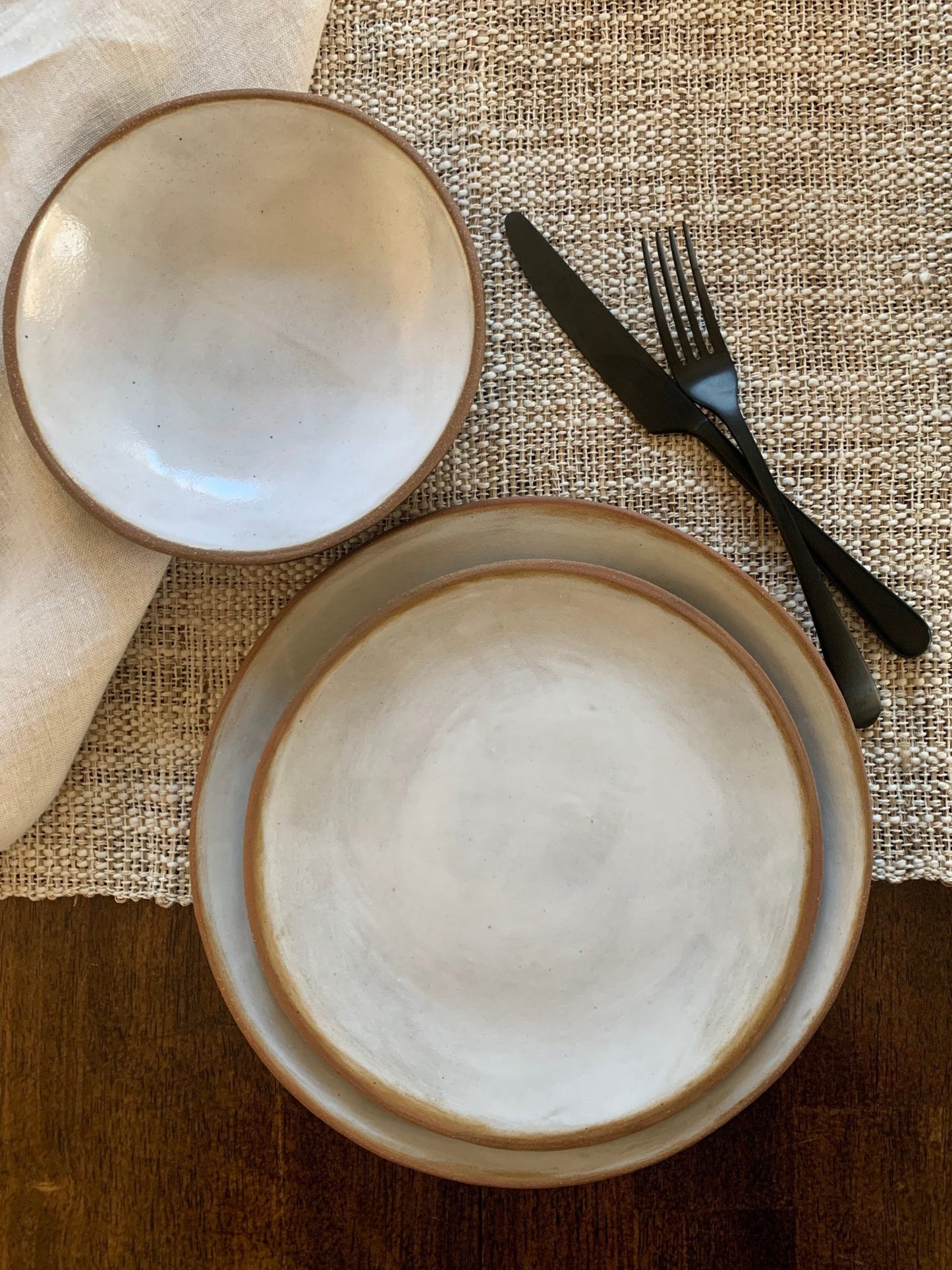 Two handmade ceramic bowls on a textured tablecloth with black cutlery.