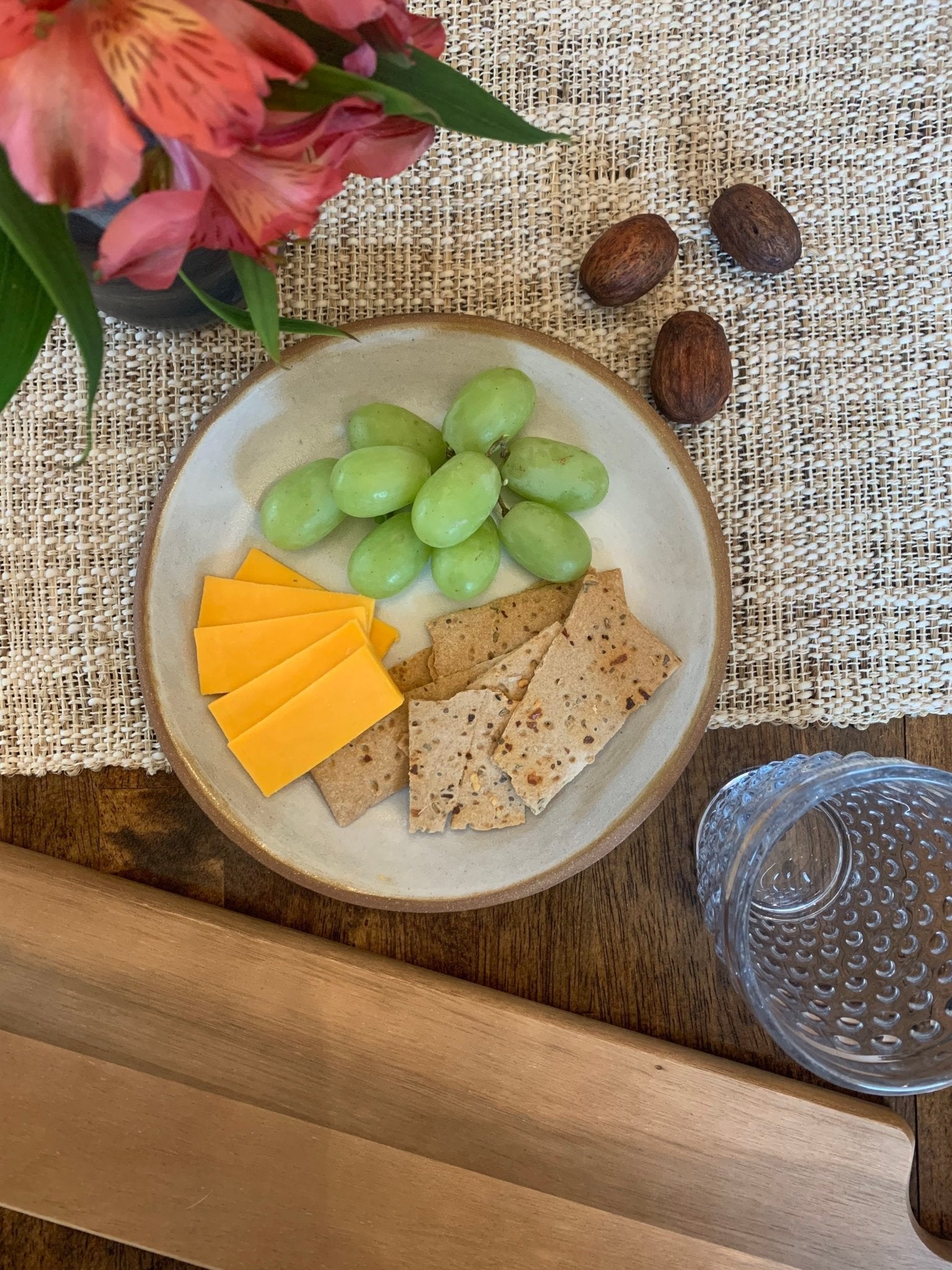 Handmade ceramic plate with cheese, crackers, and grapes on a textured tablecloth.