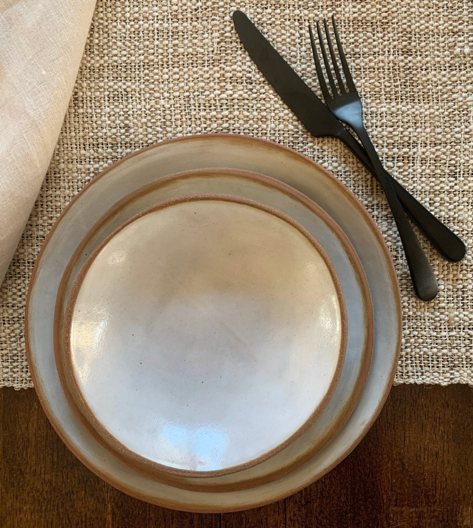 Handmade ceramic plate with black cutlery on a textured surface