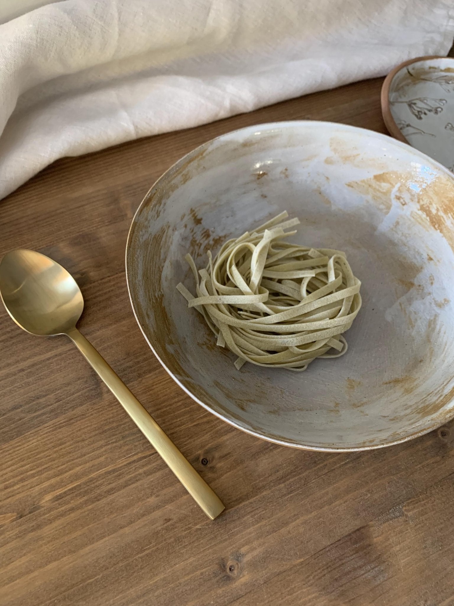 Handmade ceramic bowl with pasta on a wooden table with a gold spoon