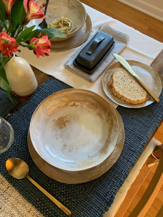 Dining table setting with handmade stoneware, bread, and flowers on a blue placemat.