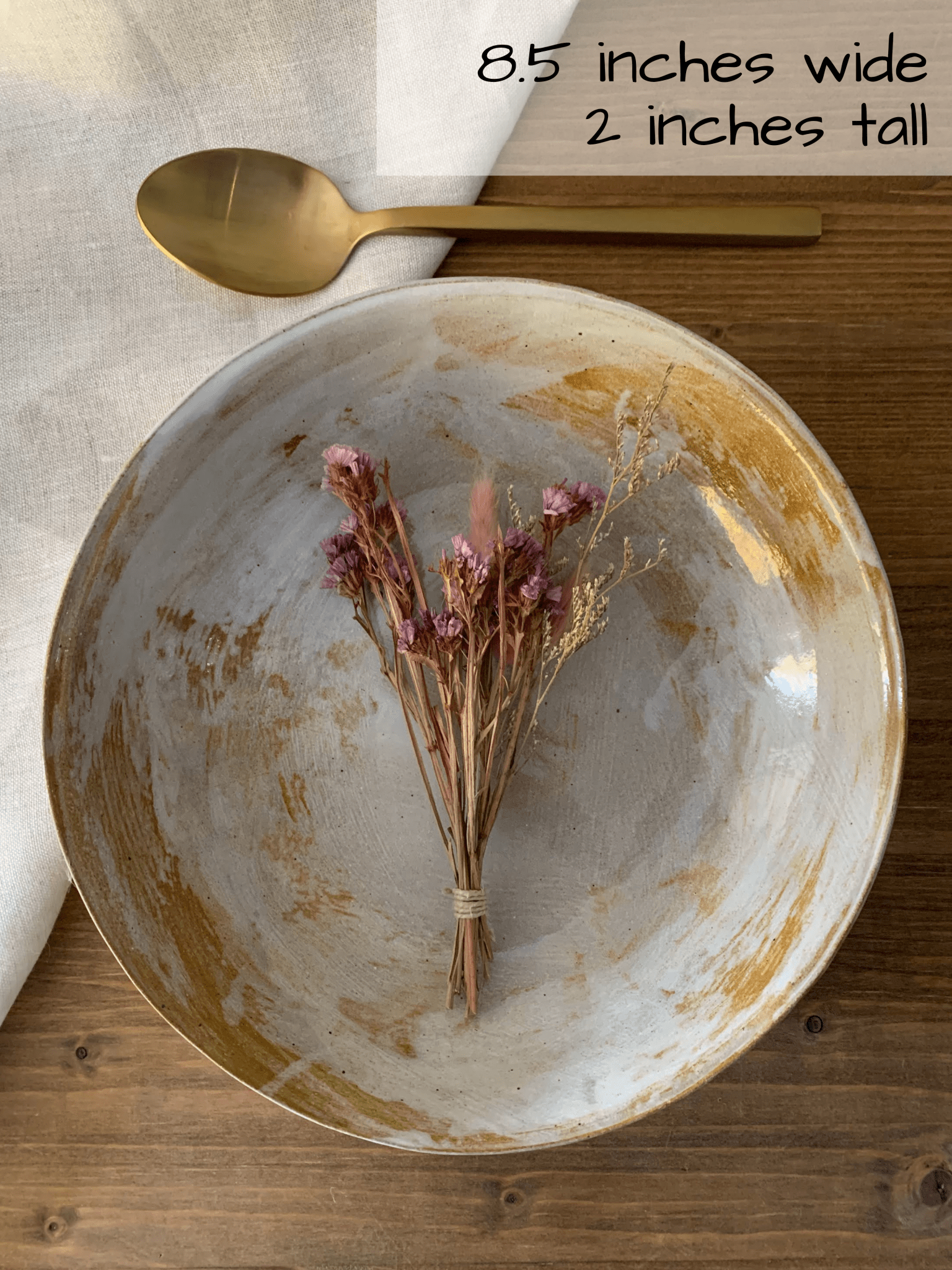 Handmade ceramic bowl and dried flowers on a wooden surface, with text indicating dimensions.