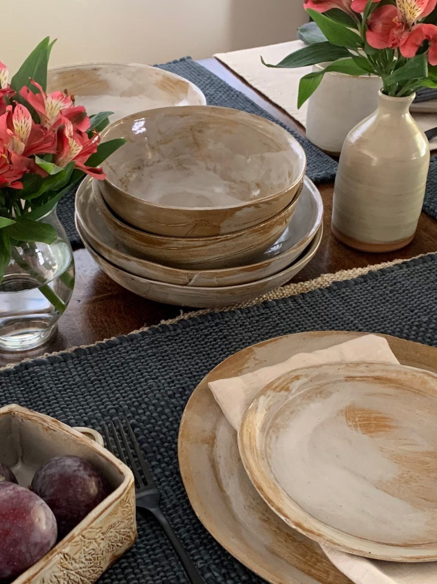 Set of handmade ceramic plates and bowls on a table with flowers and fruit