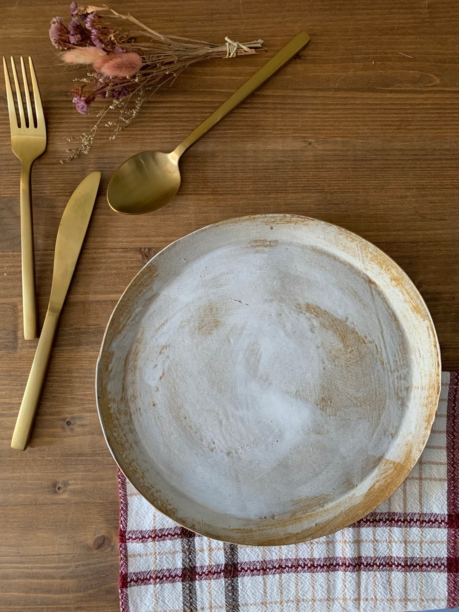 Ceramic plate on a wooden table with gold cutlery and a plaid cloth.