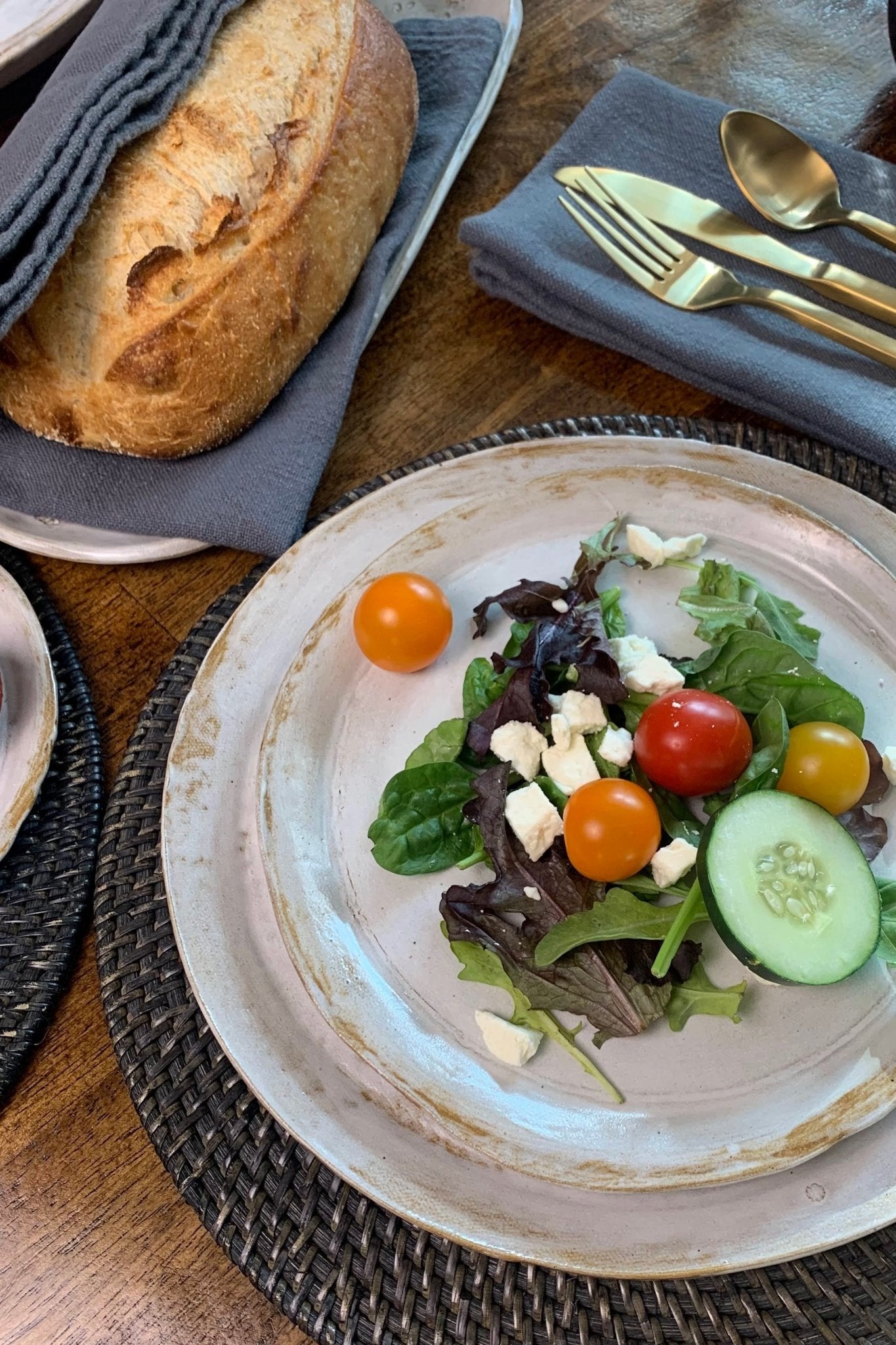 Plated salad with tomatoes and cucumbers on a wooden table with bread and cutlery.