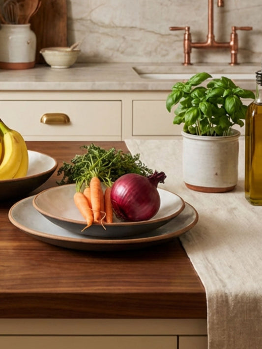 two shallow ceramic pottery bowls with carrots and an onion in the top one on a wood countertop in a kitchen