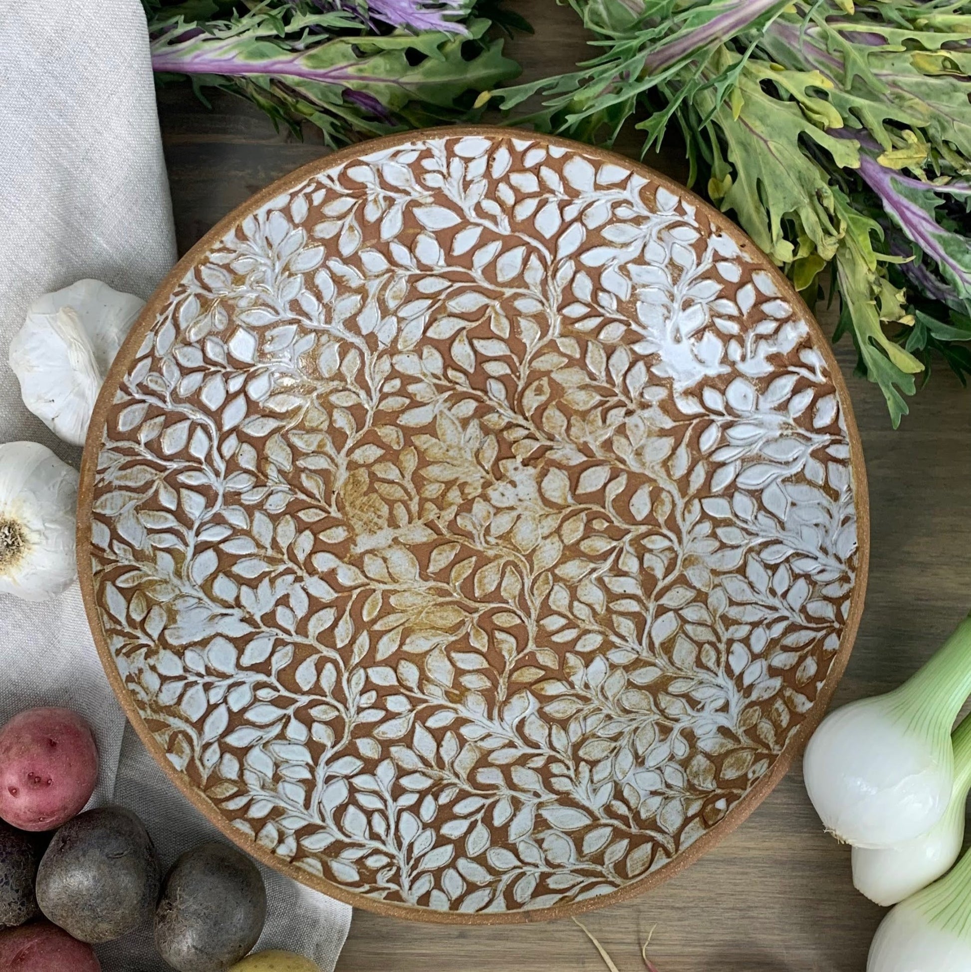 Decorative ceramic plate with floral pattern on a wooden surface with vegetables.