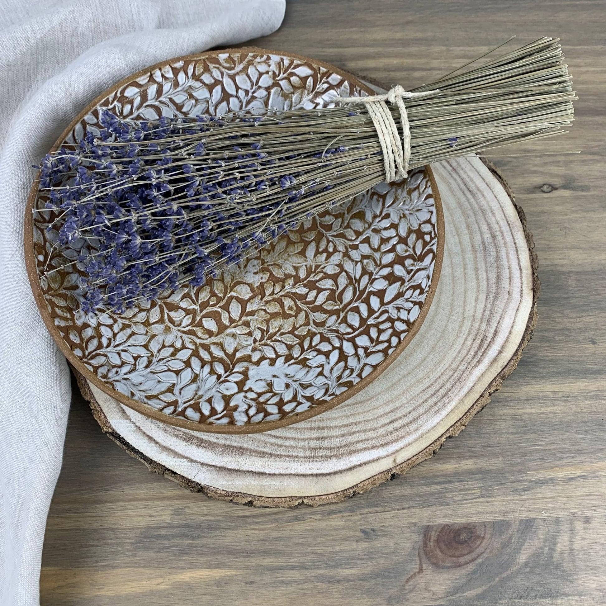 Handmade decorative ceramic plate with floral patterns, lavender, and a broom on a wooden surface.