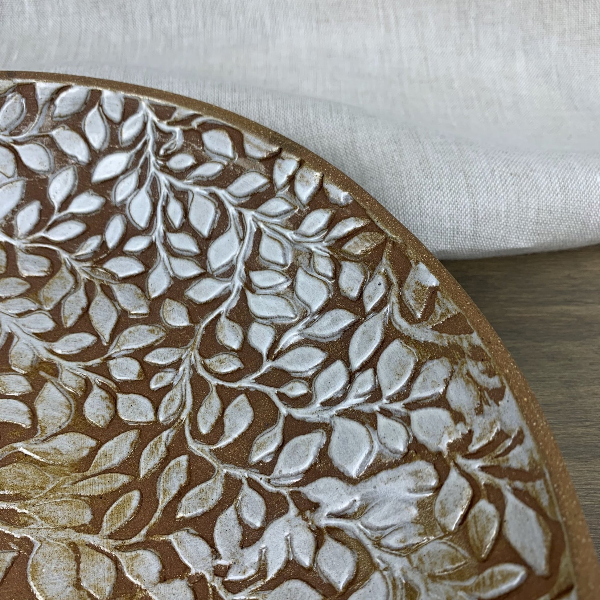 Close-up of a handmade ceramic plate with leaf pattern on a white background