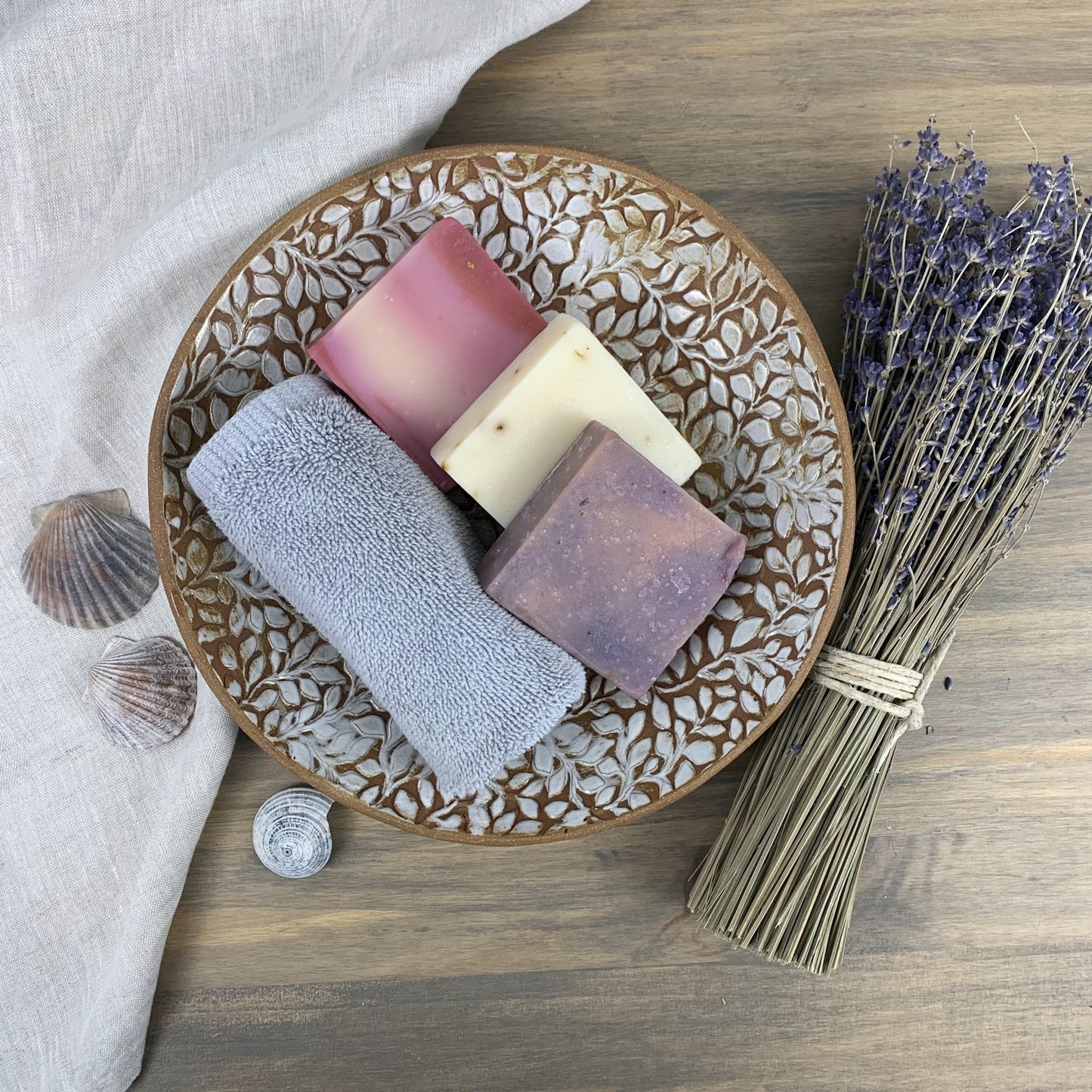 Decorative ceramic plate with soaps and a bundle of lavender on a wooden surface