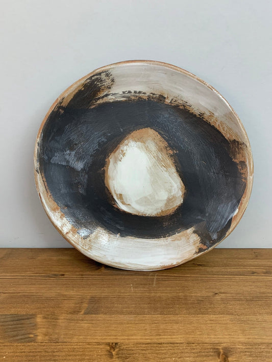 Ceramic art bowl with expressive black and white brush strokes leaning on a gray wall