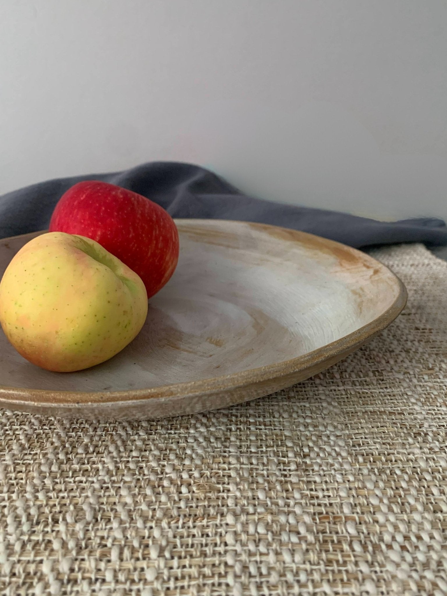 Two apples on a handmade ceramic plate with a gray napkin and textured surface