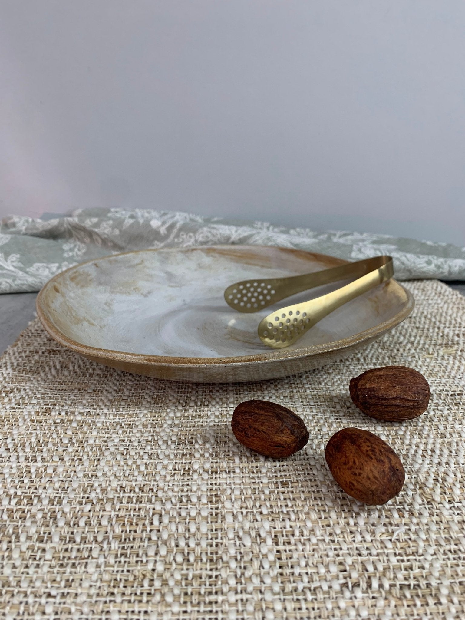 Decorative handmade ceramic plate with gold tongs and almonds on a textured surface