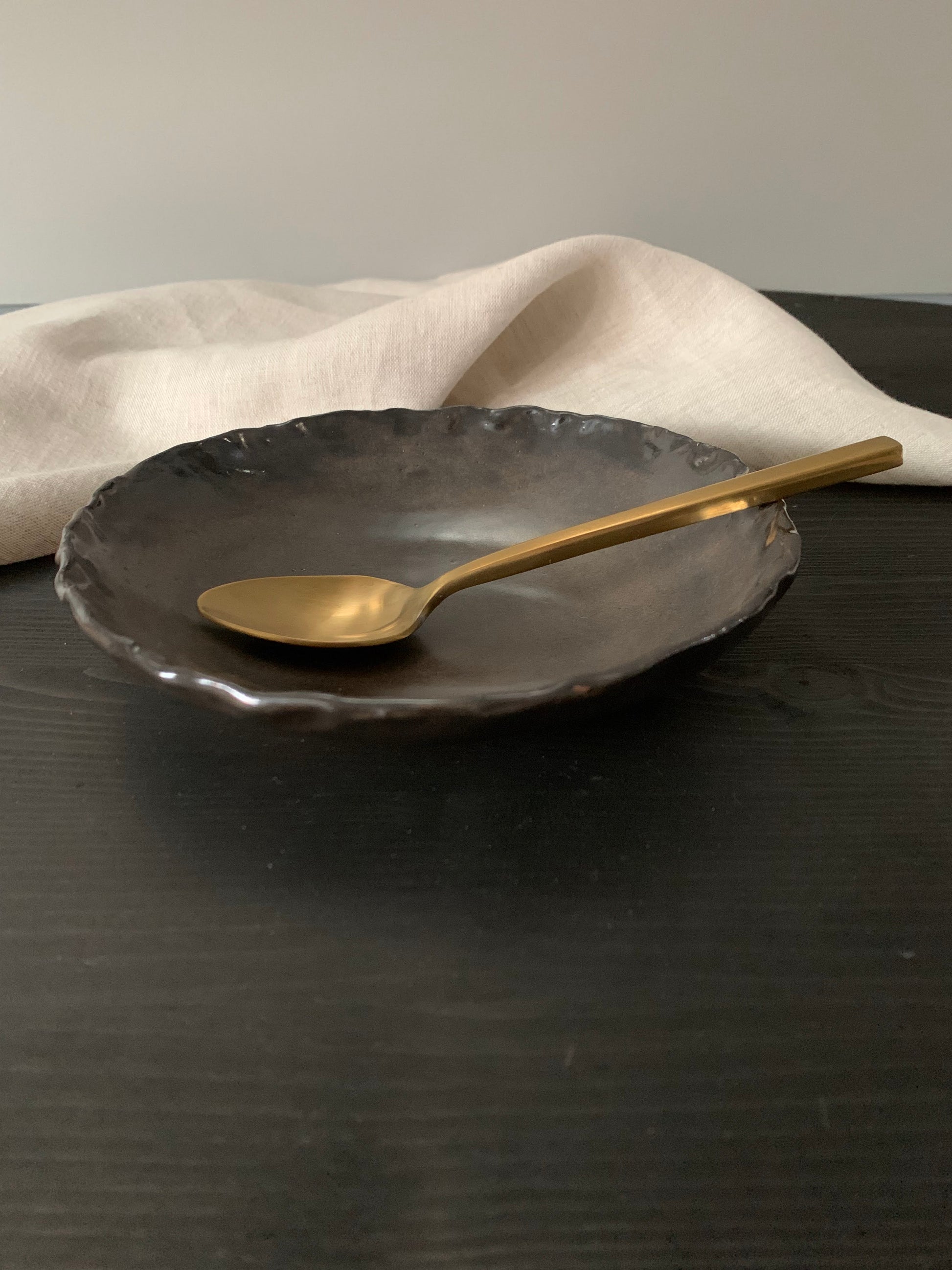 Gold spoon in a dark brown handcrafted ceramic side bowl with a neutral background