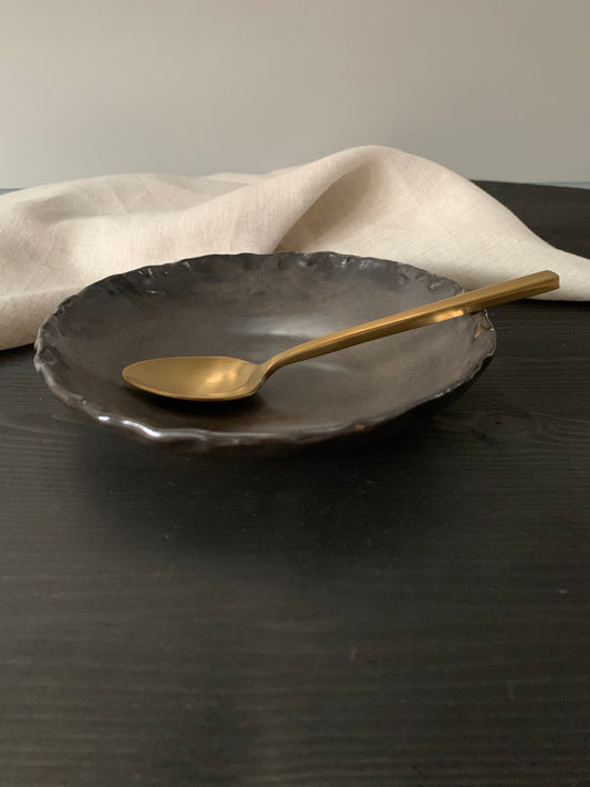 Gold spoon in a dark brown handcrafted ceramic side bowl with a neutral background