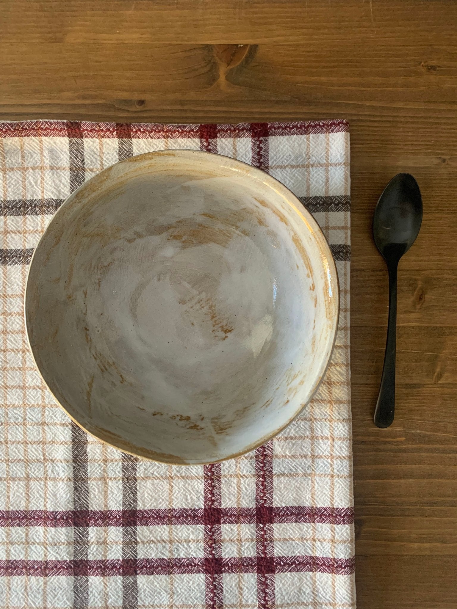 Handmade ceramic bowl and spoon on a checkered cloth with wooden surface
