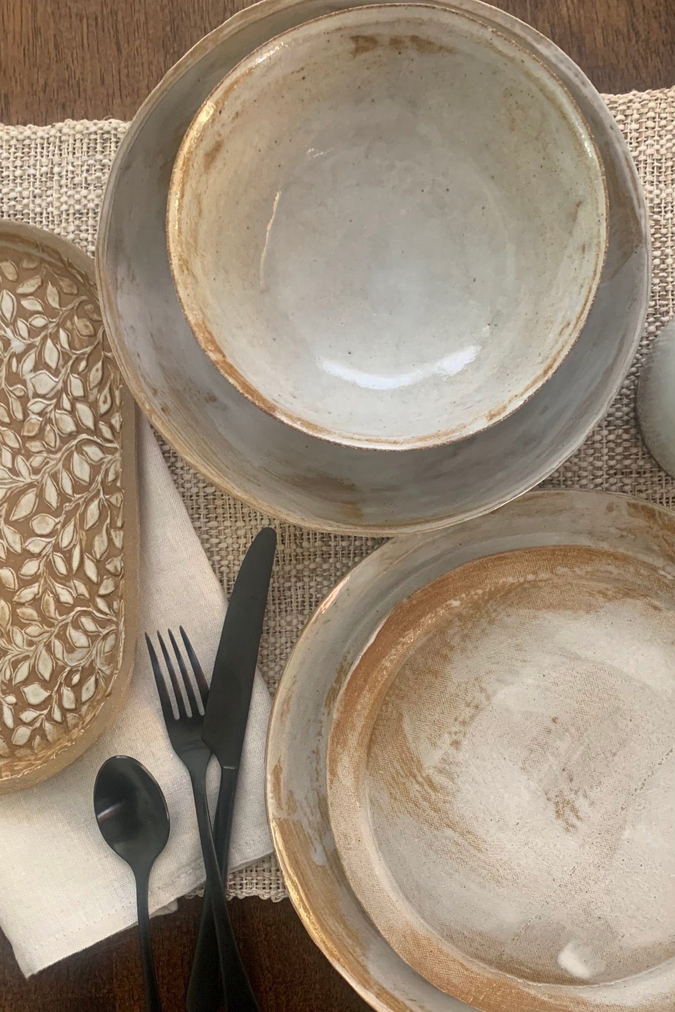 Set of handmade ceramic bowls on a textured tablecloth with cutlery.