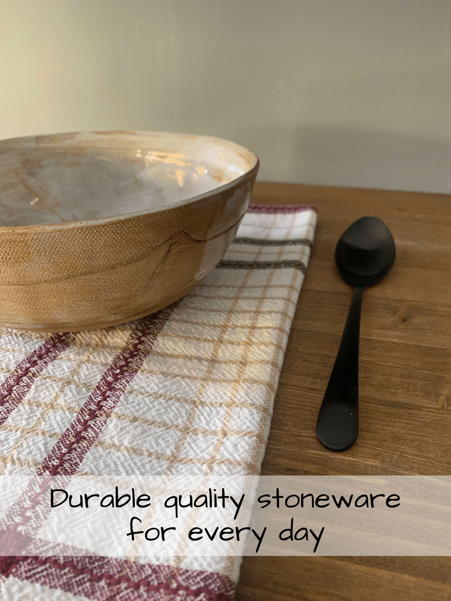 Stoneware bowl and black spoon on a wooden surface with a plaid cloth, text 'Durable quality stoneware for every day'.