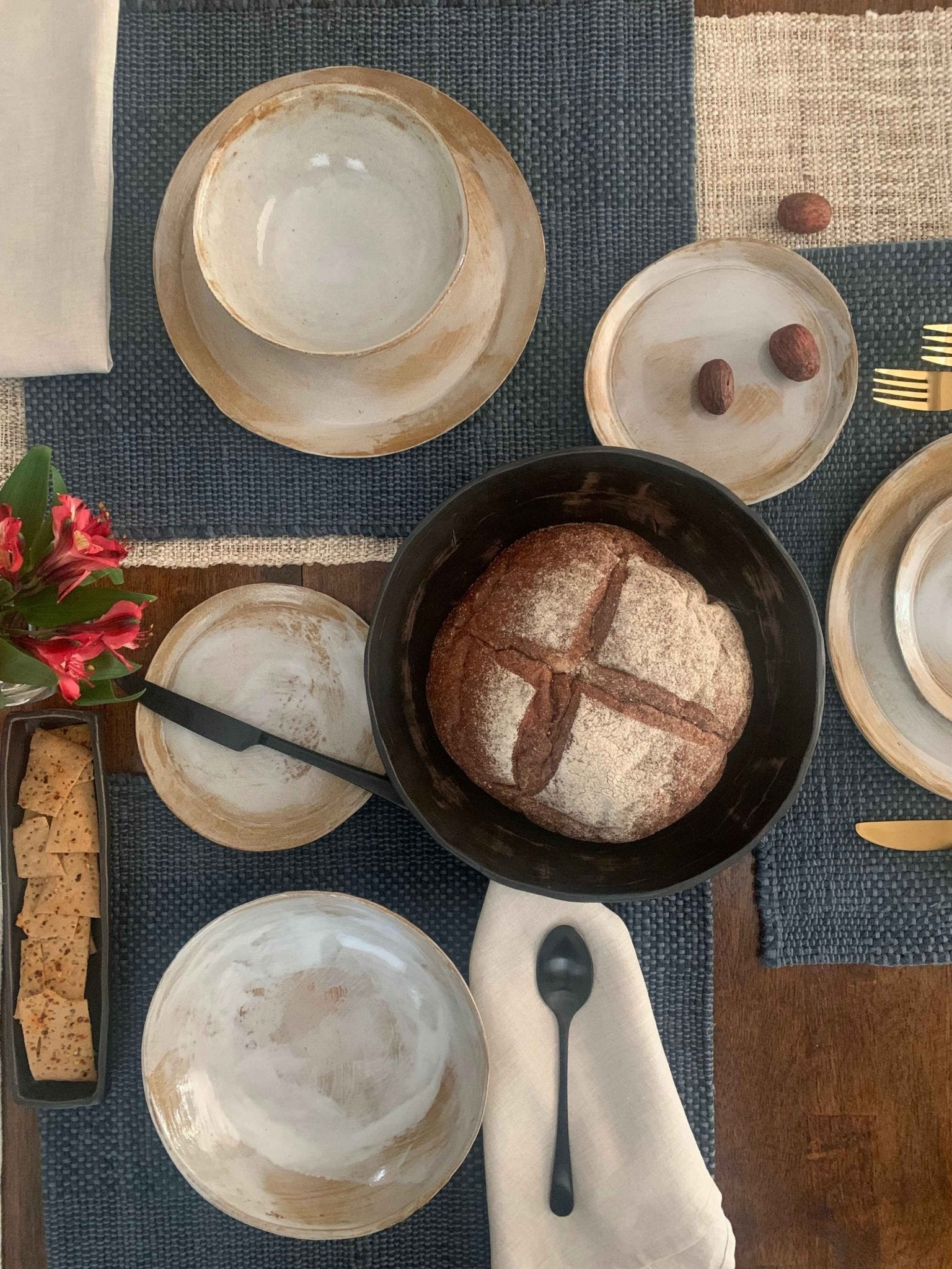 Table setting with handmade ceramic dinnerware, and utensils on a blue placemat.
