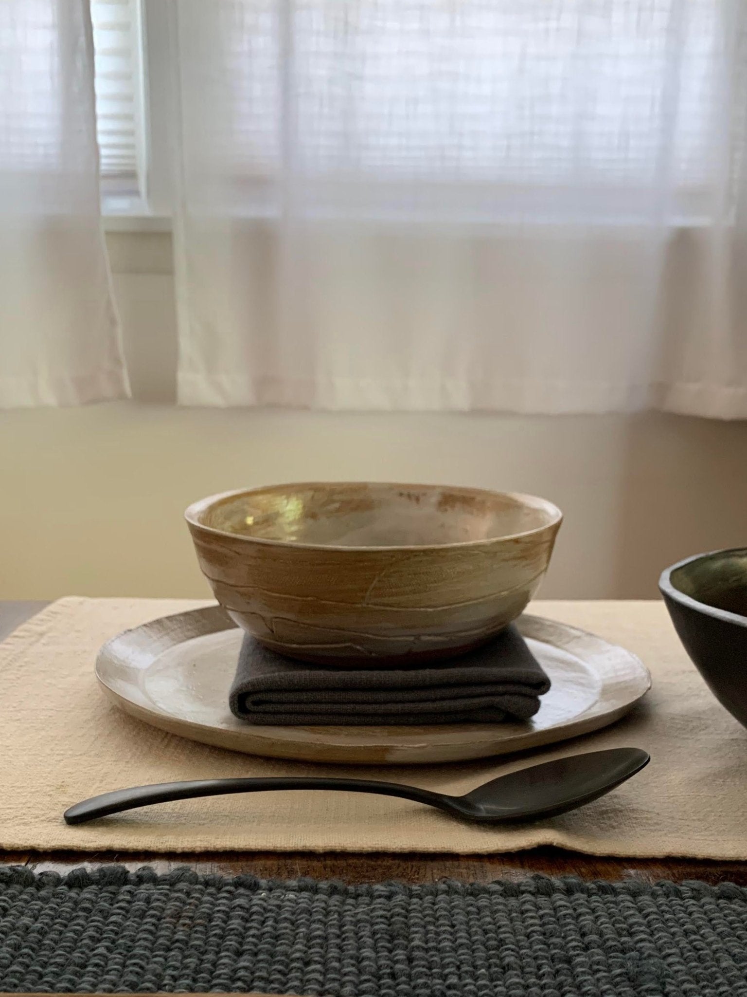 Handmade ceramic bowl, plates, and spoon on a table with a neutral background