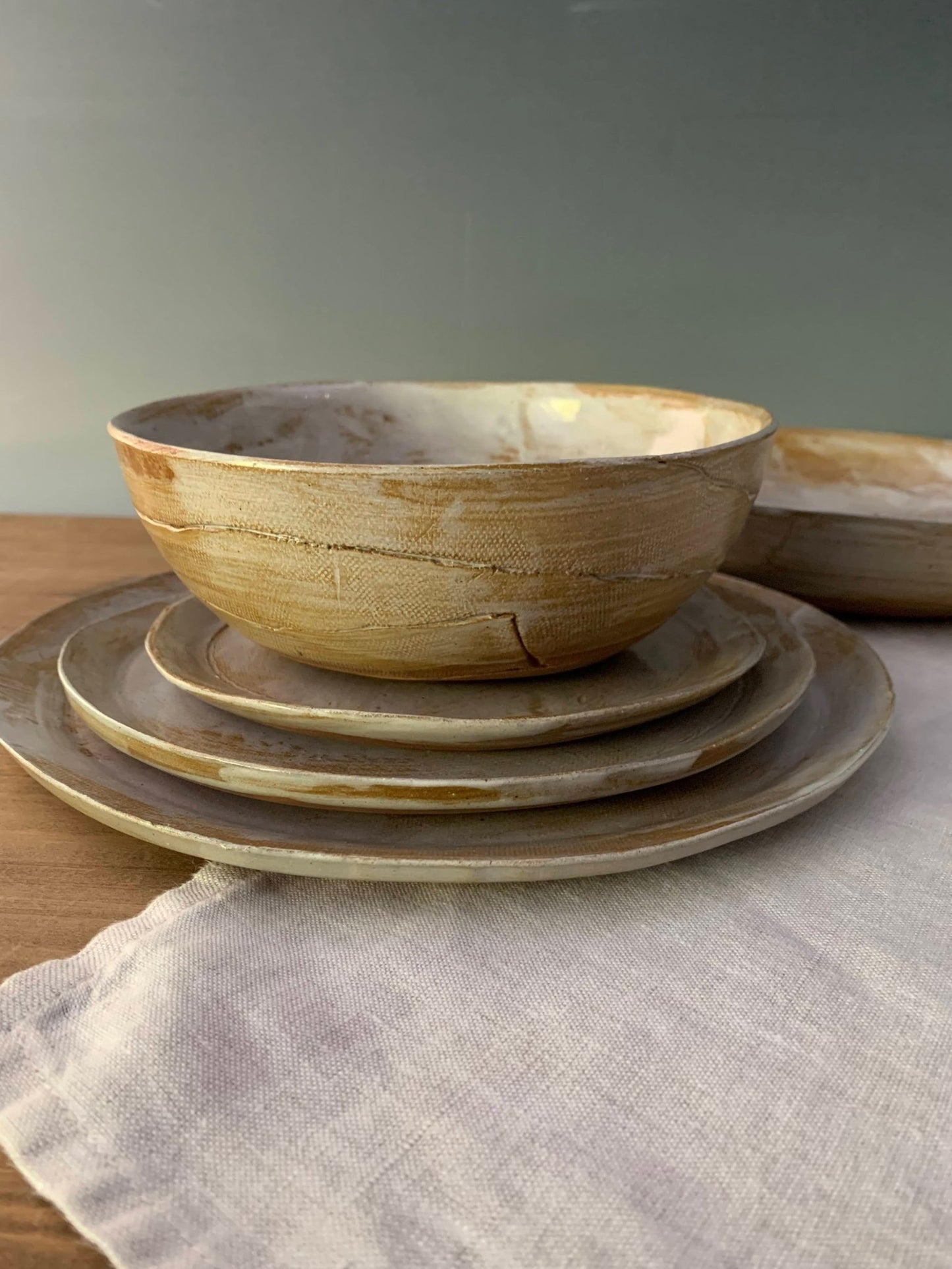 Stack of 3 hand formed plates and a soup bowl on top as a place setting on a wood table