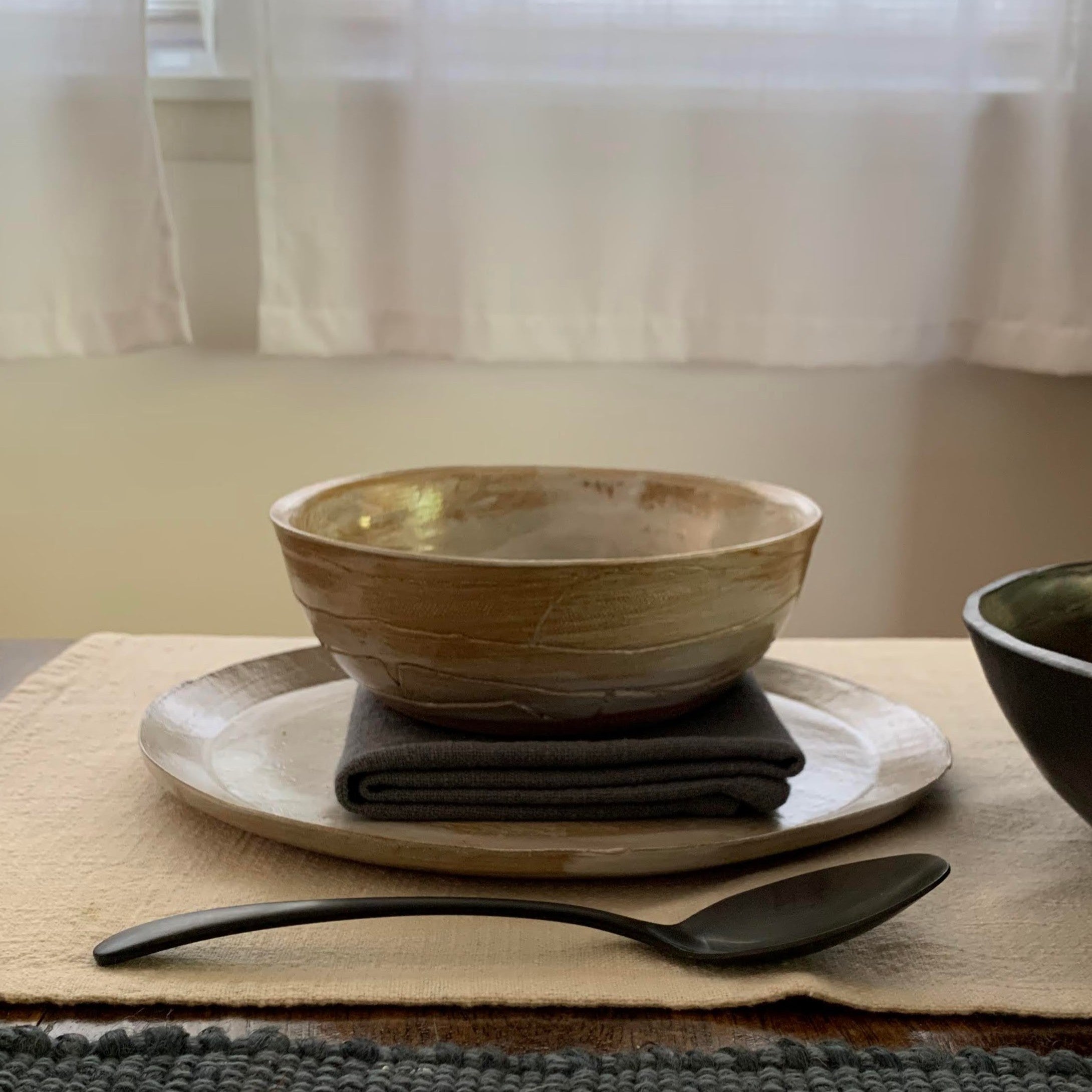 Ceramic bowl, plate, and spoon on a table with a neutral background