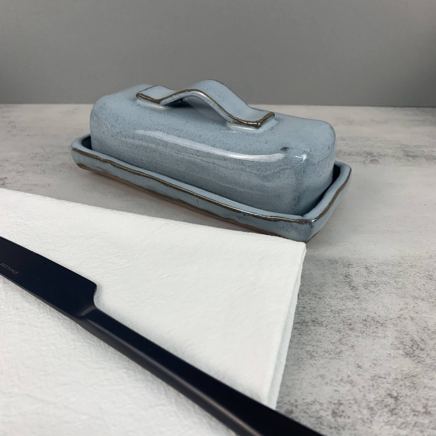 Blue ceramic butter dish on a marble surface with a gray background
