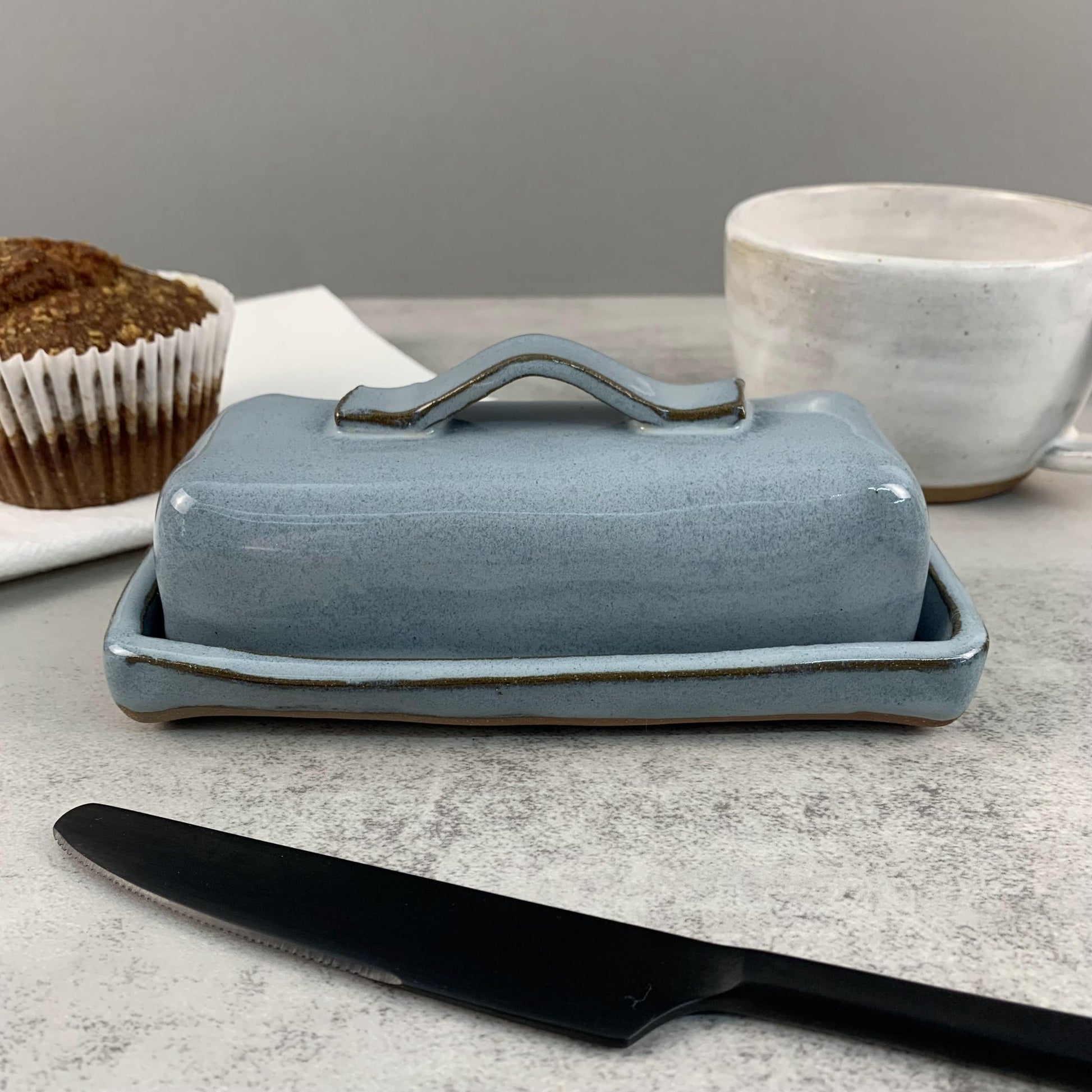 Blue ceramic butter dish with a black knife on a gray surface.
