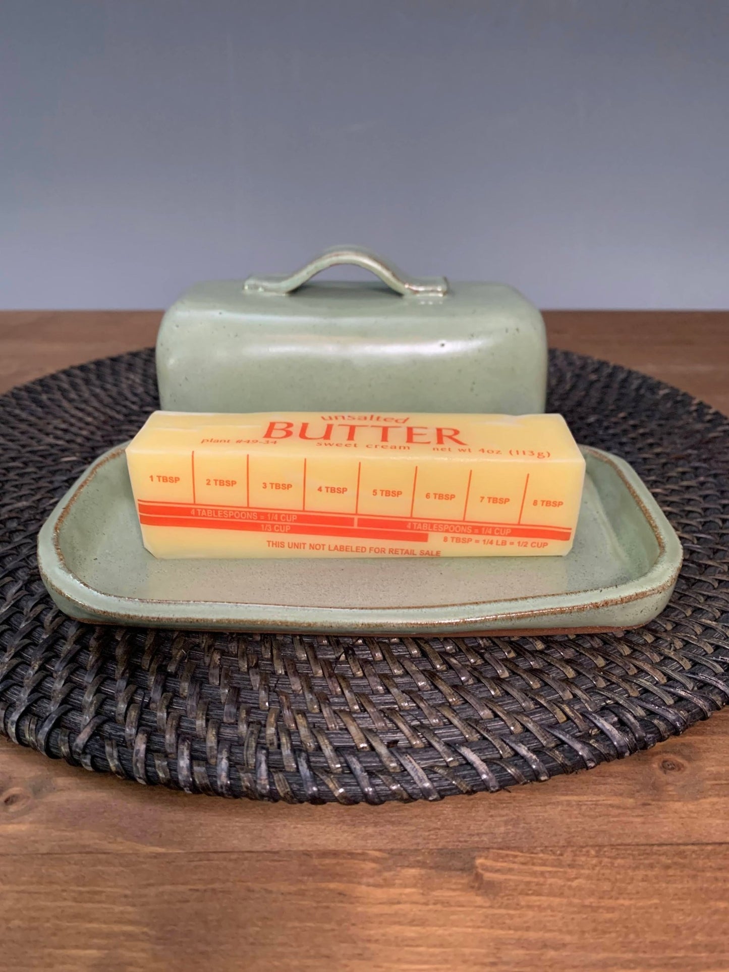 green Handmade ceramic Butter dish with a stick of butter on a woven mat, gray background