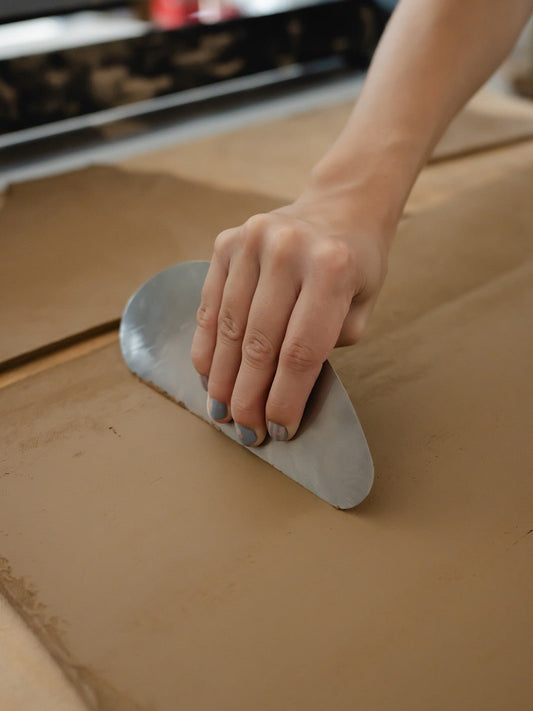 Hand using a pottery tool on a slab of wet clay  in a ceramic art studio