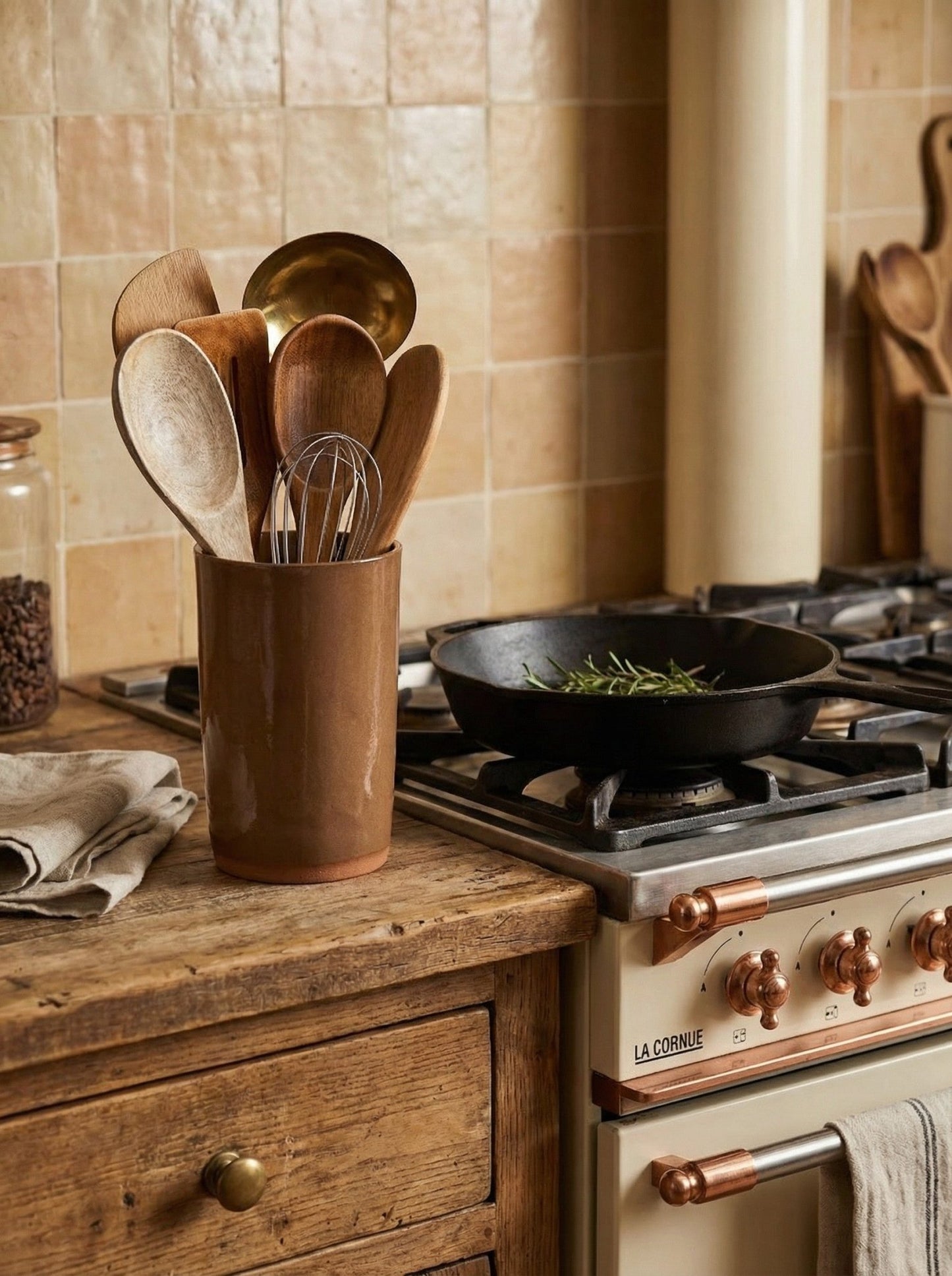 Wooden utensils in a artisan crafted CERAMIC holder on a kitchen counter with a stove and pan in the background.