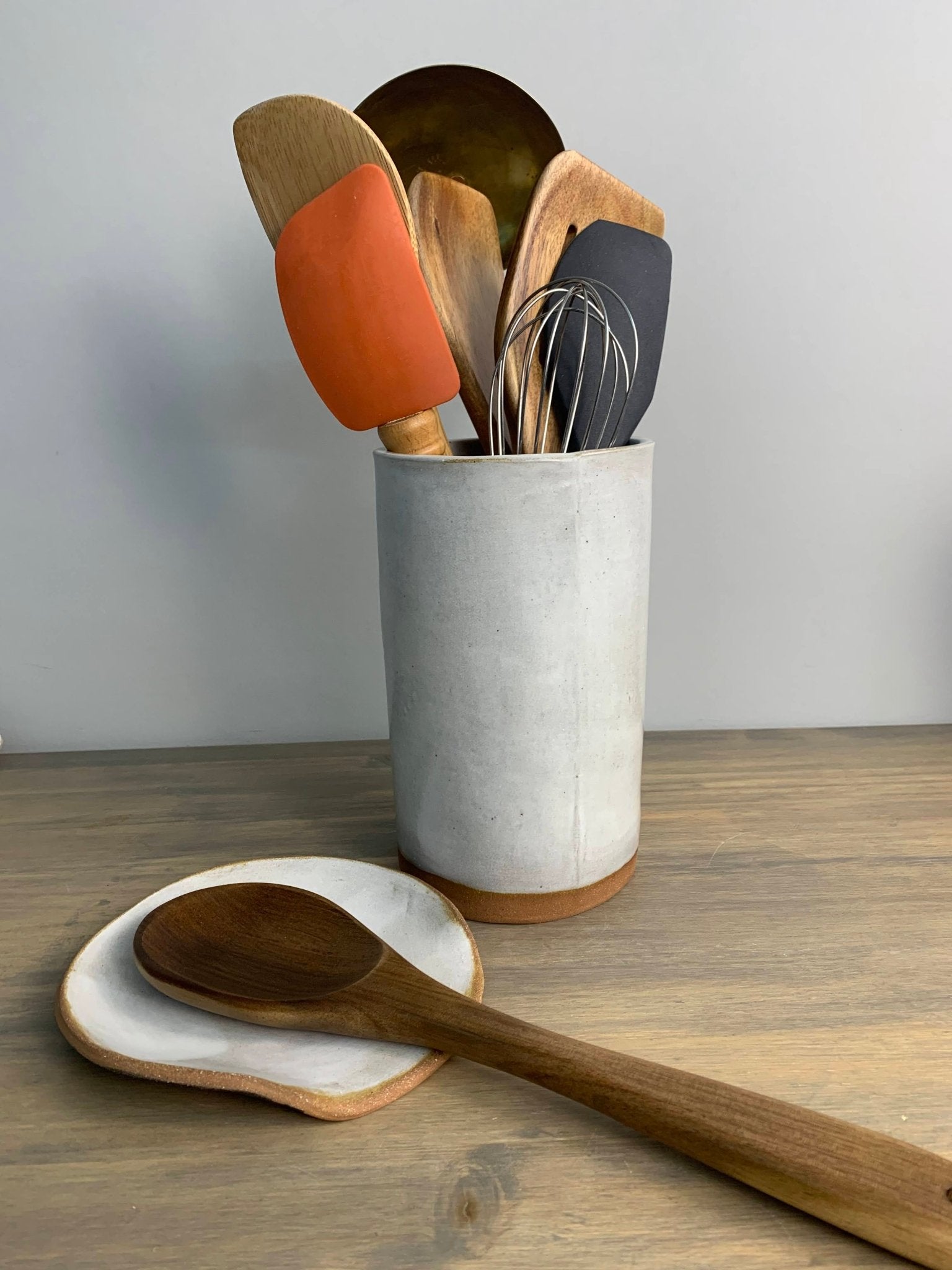 Set of wooden utensils in a handmade pottery utensil holder on a wooden surface.