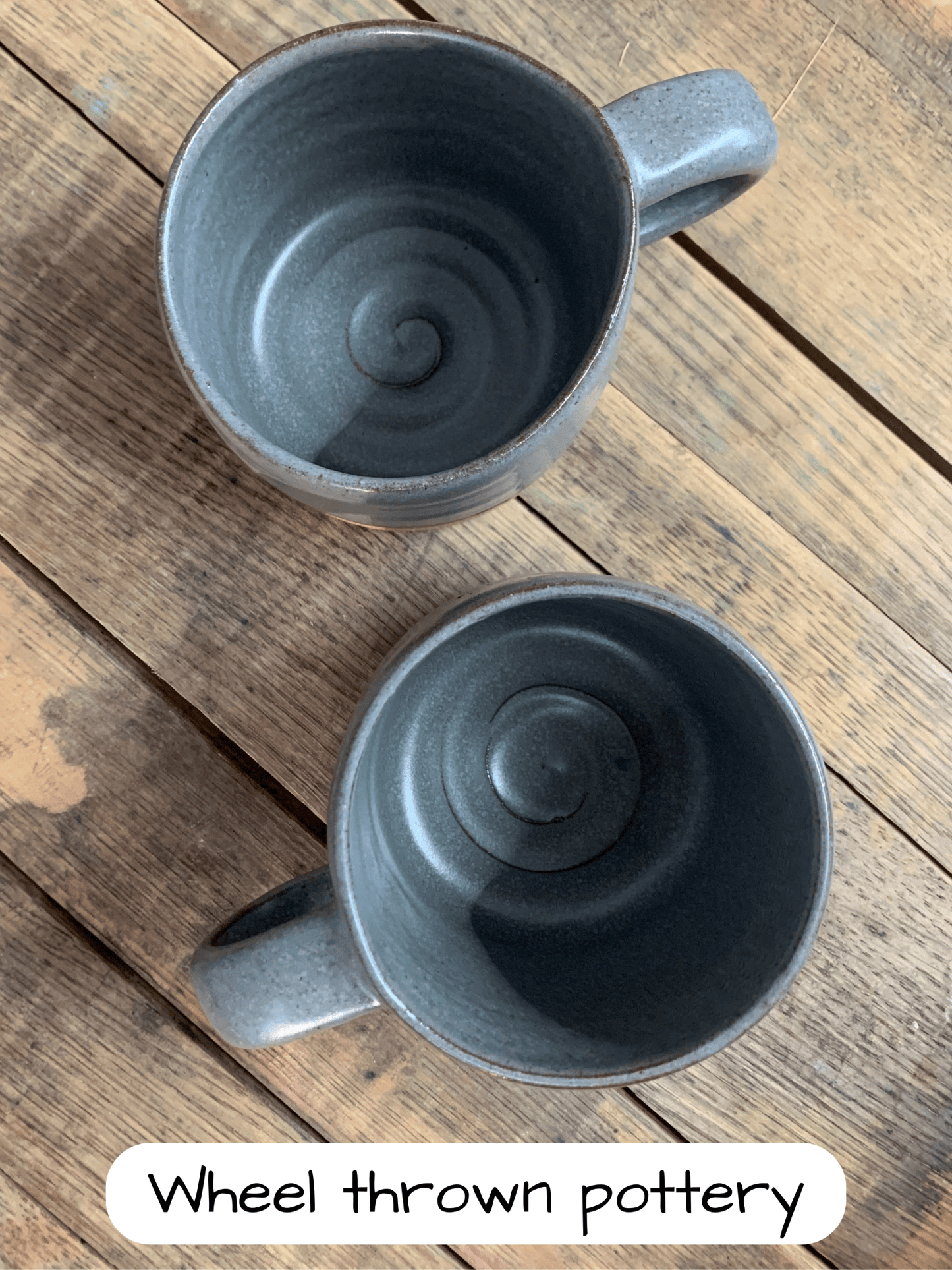 Two gray ceramic mugs on a wooden surface with 'Wheel thrown pottery' text.