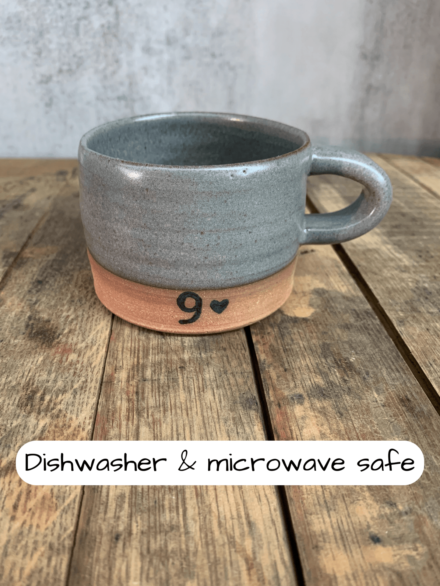 Gray ceramic mug with terracotta base on a wooden surface, labeled 'Dishwasher & microwave safe'.