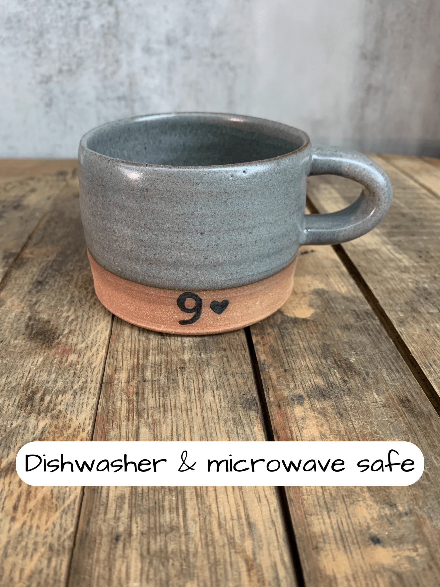 Gray ceramic mug with terracotta base on a wooden surface, labeled 'Dishwasher & microwave safe'.