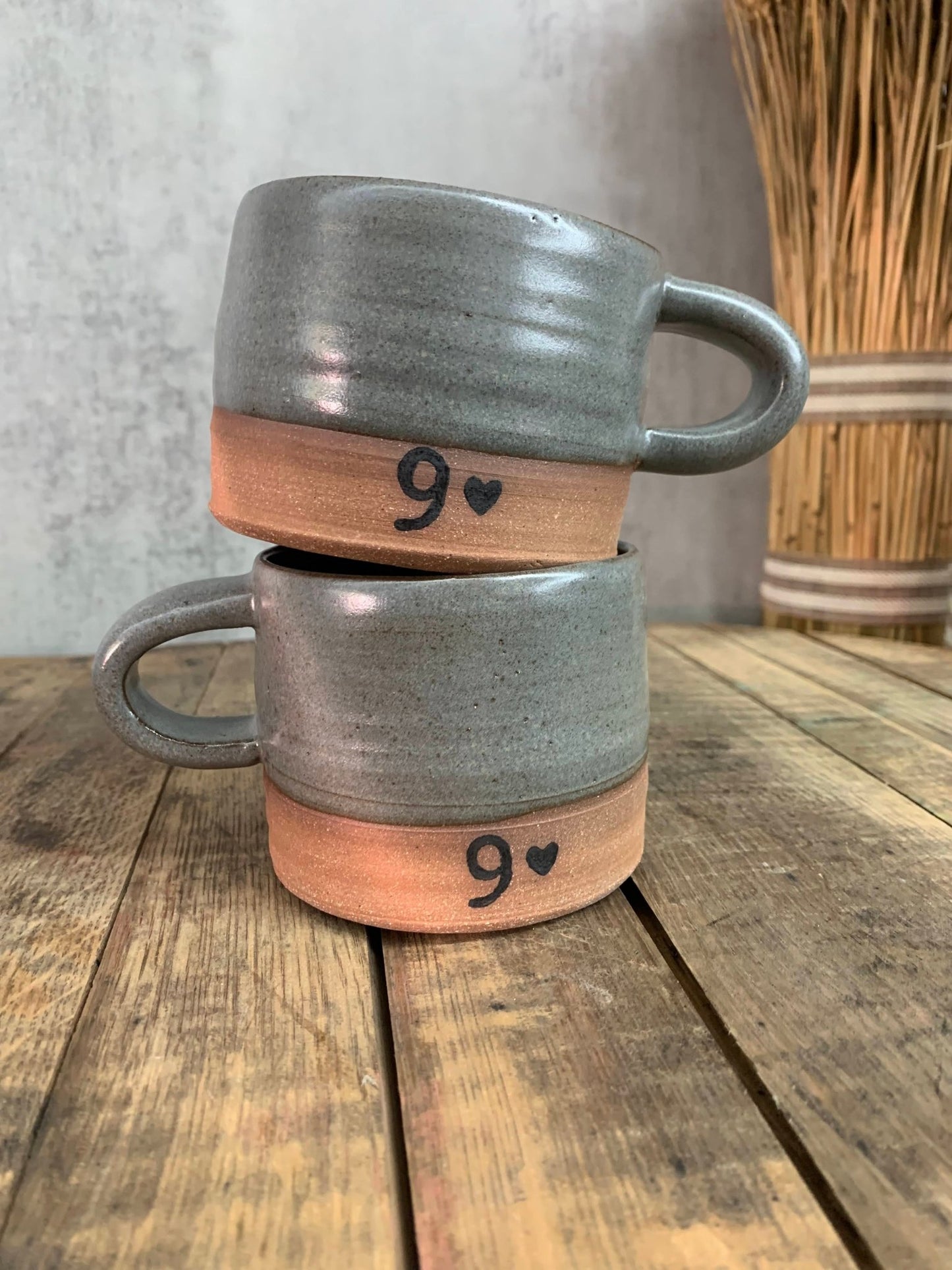 Two gray mugs stacked on top of each other with wooden bases, featuring the number 9 and a heart symbol, on a wooden surface.