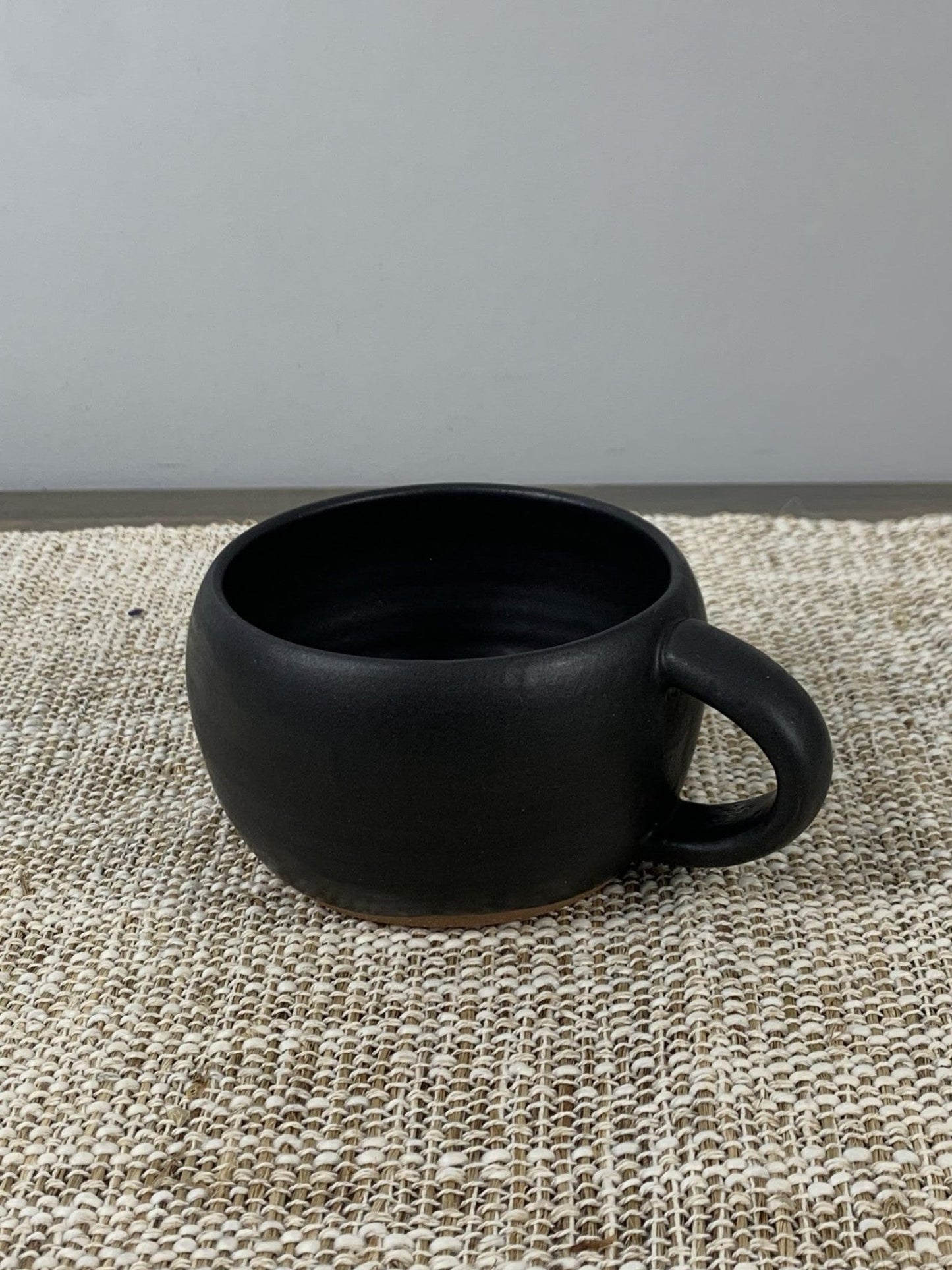 Black handcrafted latte mug on a textured surface with a neutral background