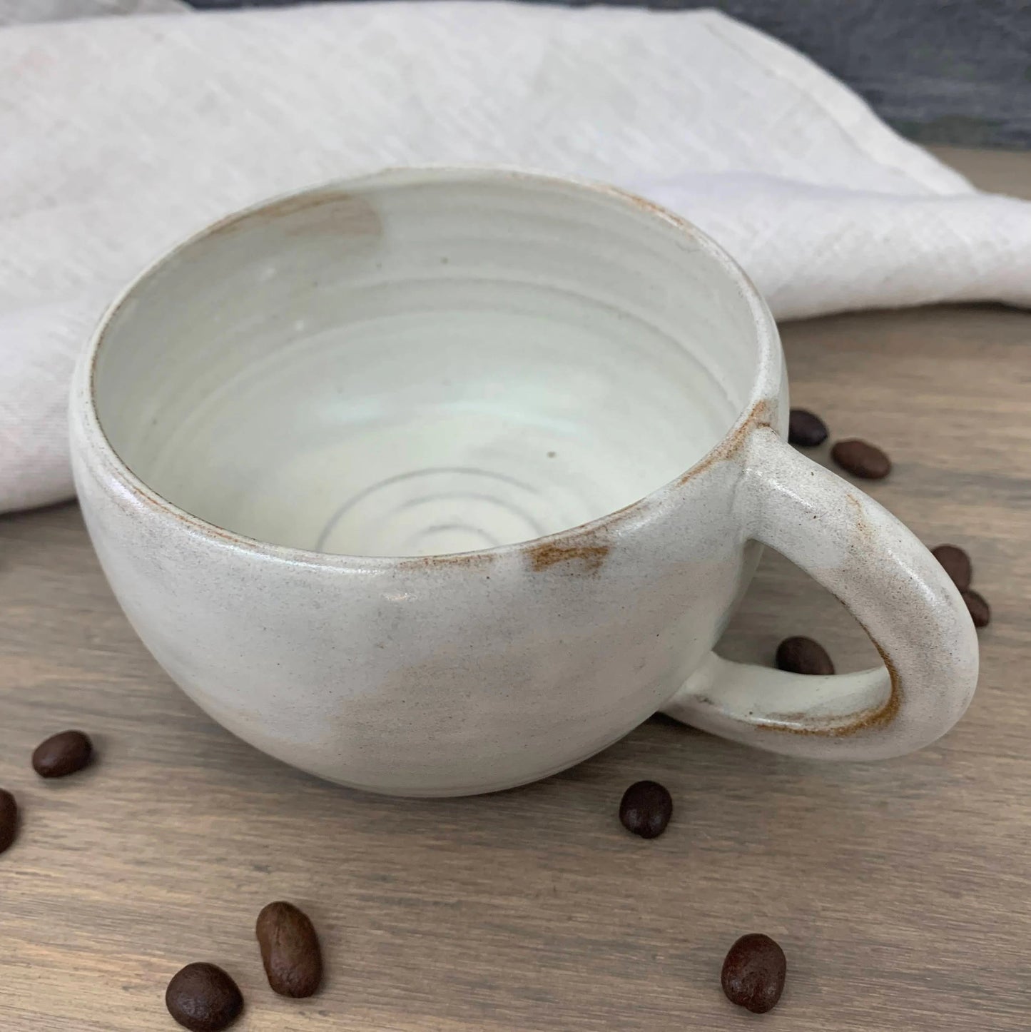 White ceramic mug on a wooden surface with scattered coffee beans
